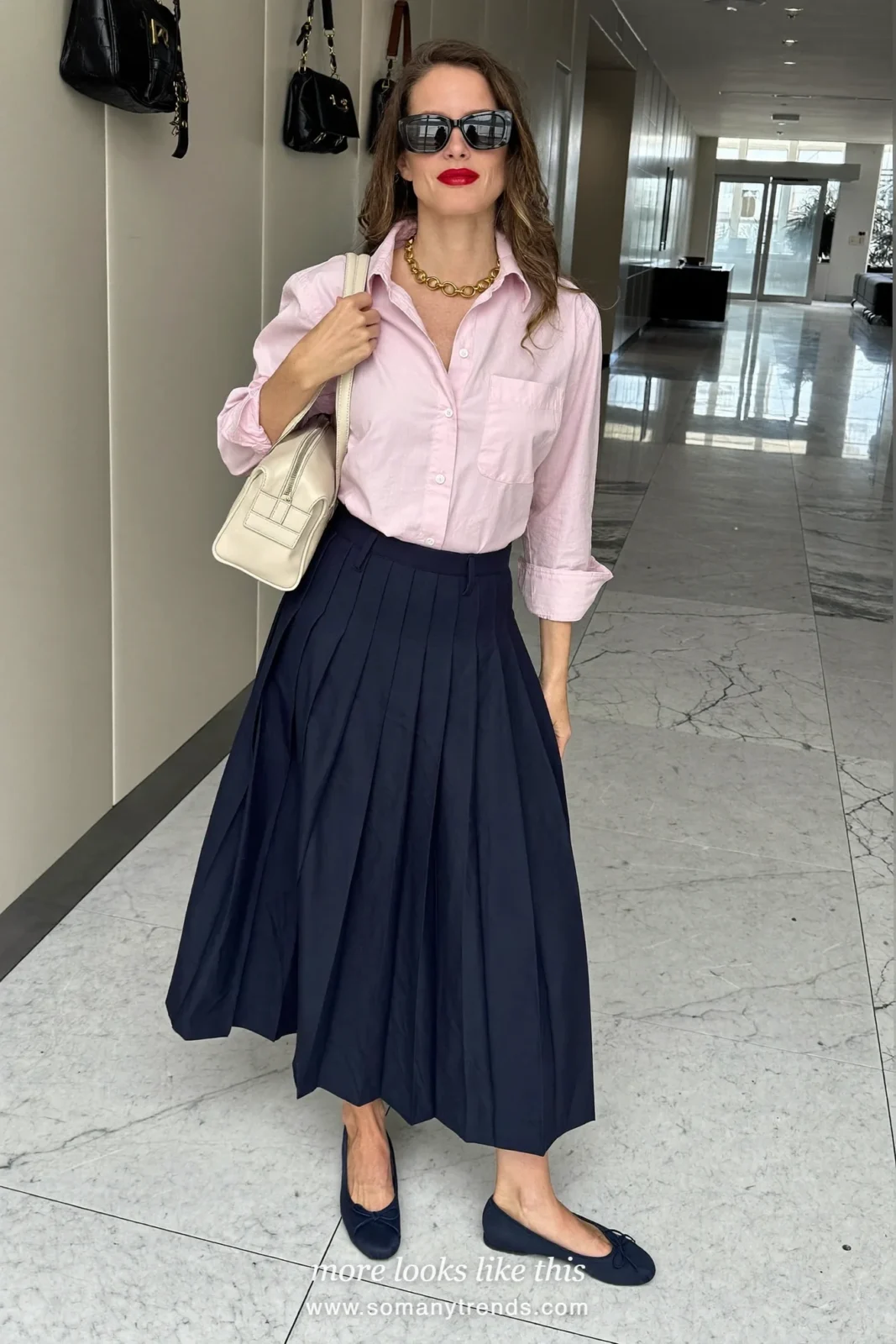 Woman in a pale pink oxford shirt, navy blue pleated midi skirt and navy ballet flats, outfit 2