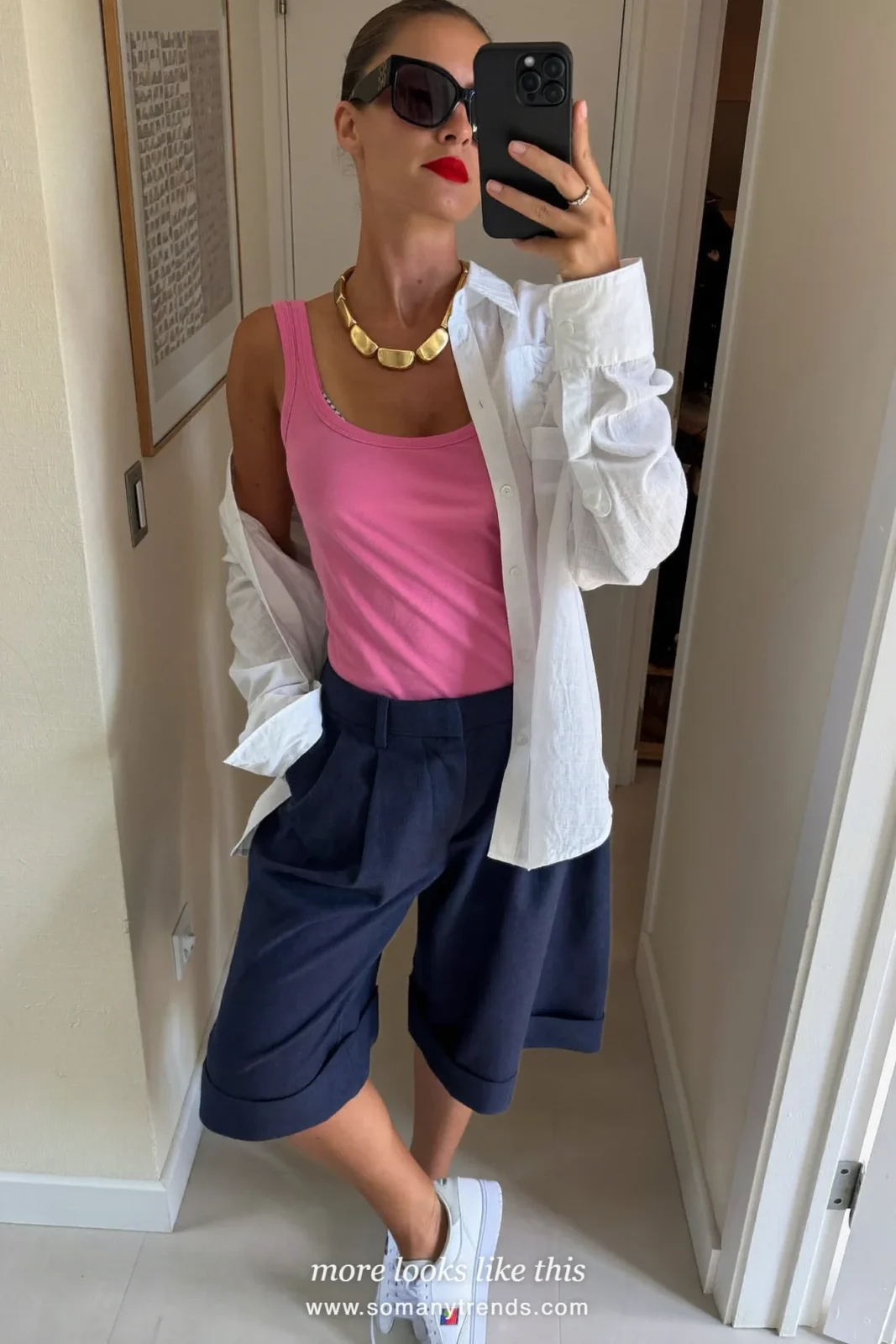Woman in long navy blue bermuda shorts, baby pink tank, open white linen shirt and white sneakers, outfit 18