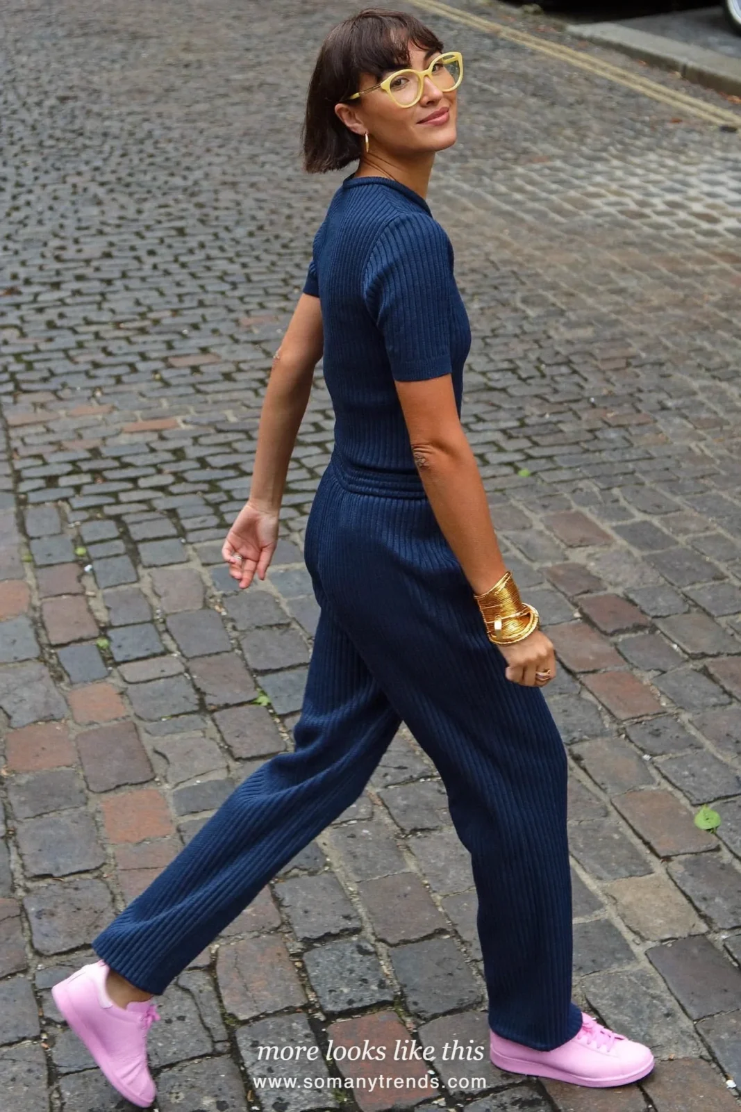 Woman in a navy blue matching top and wide pants set with baby pink sneakers and a cream bag, outfit 20