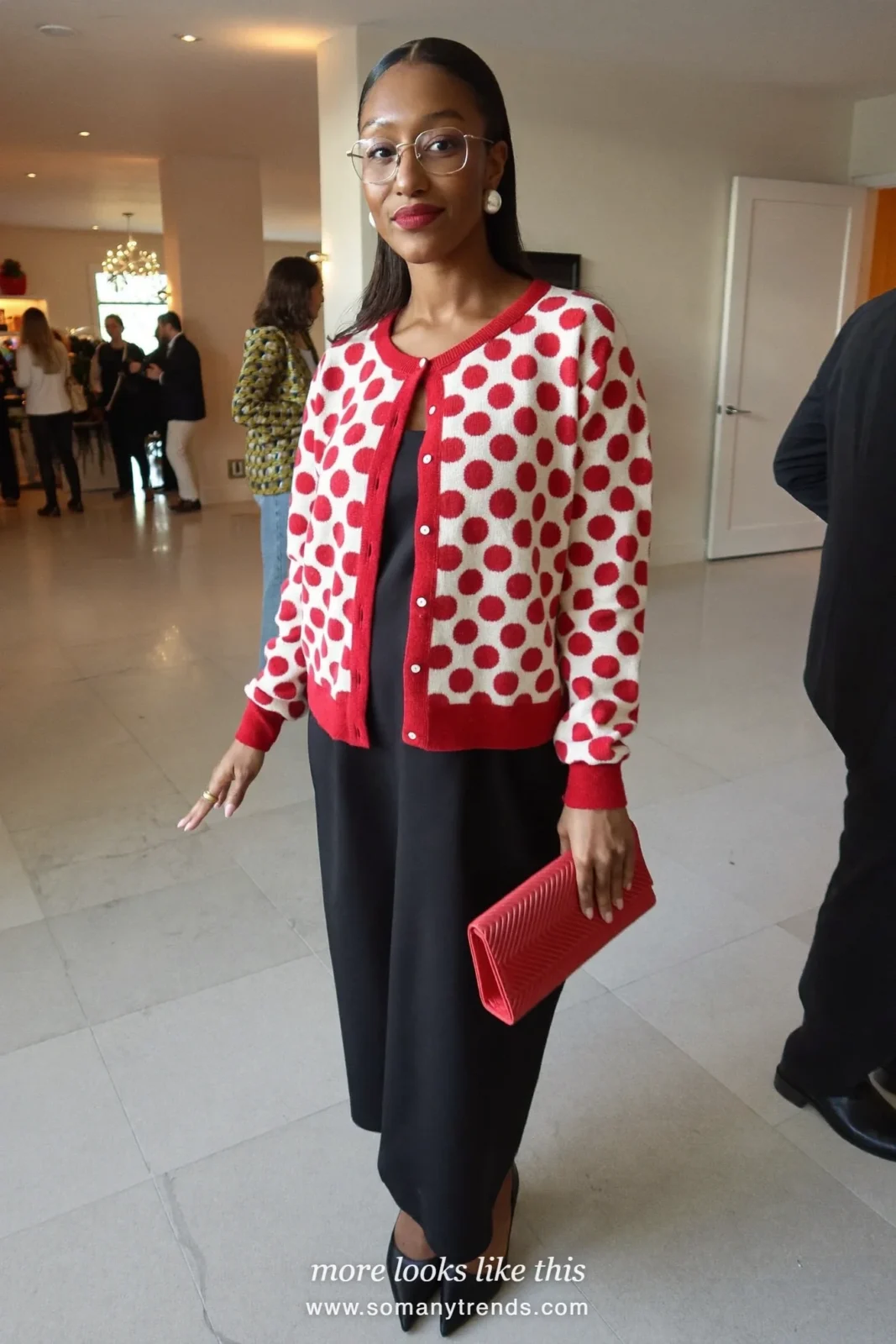 Red polka-dot cardigan buttoned over a black slip dress with black opaque tights and pointed pumps, outfit 16