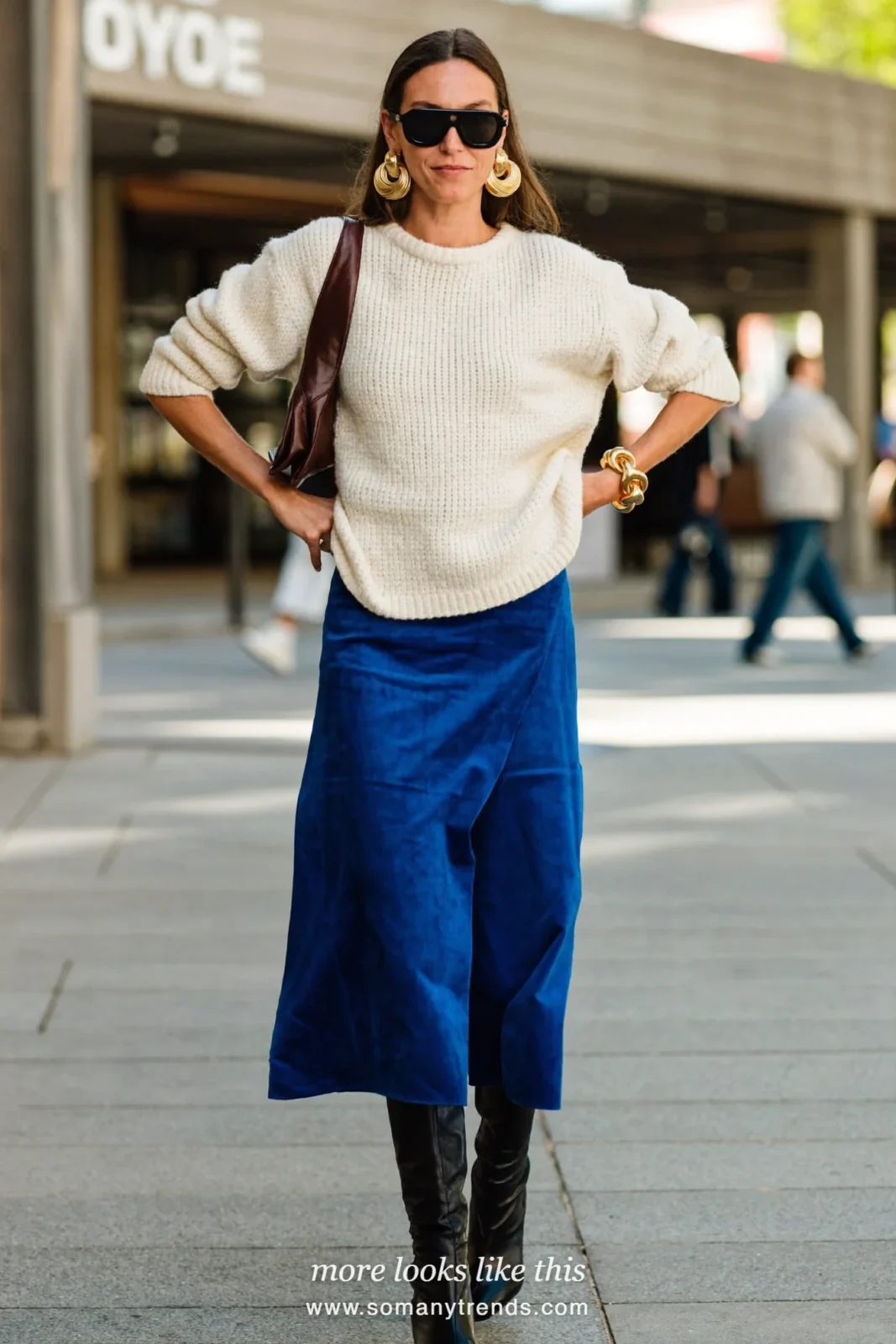 Woman in a cobalt blue velvet midi skirt, cream sweater and tall black boots, outfit 13