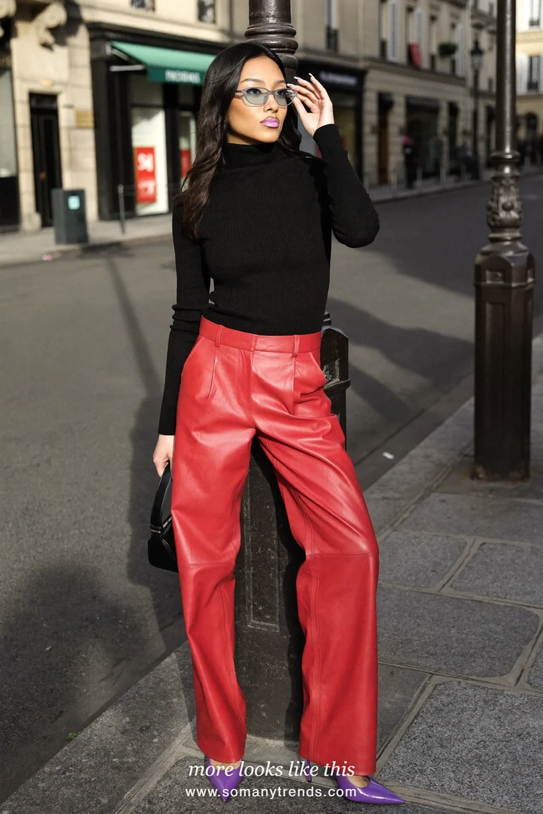 Woman in a black turtleneck, red soft matte leather straight pants, violet patent pointed pumps and a small black bag, look 17