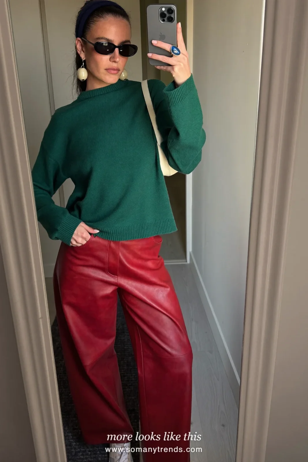 Woman in a relaxed emerald green knit, red soft matte leather straight pants, cream sneakers and a cream bag, look 21