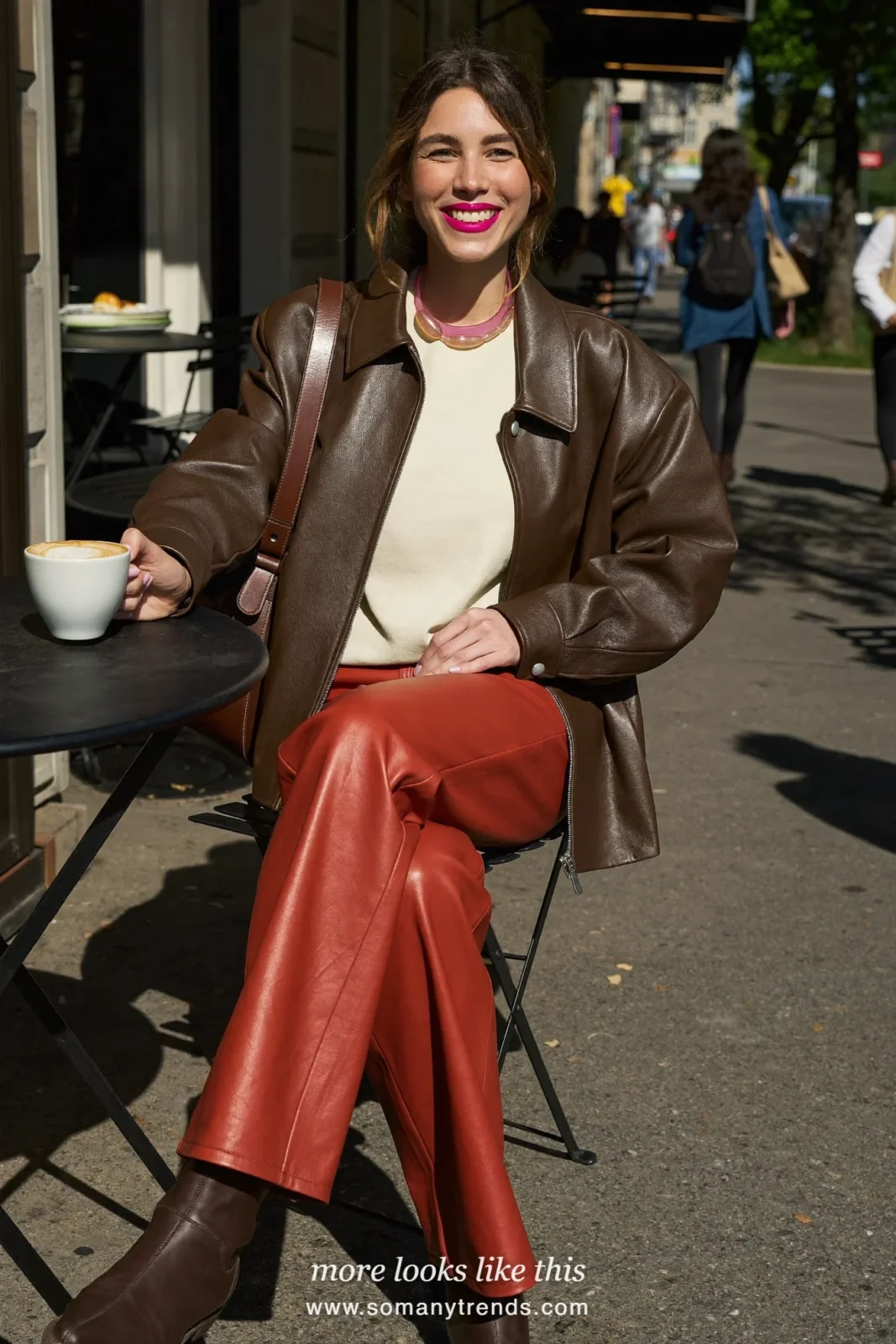 Woman in a chocolate brown leather jacket over a cream tee, red soft matte leather straight pants and brown ankle boots, look 23
