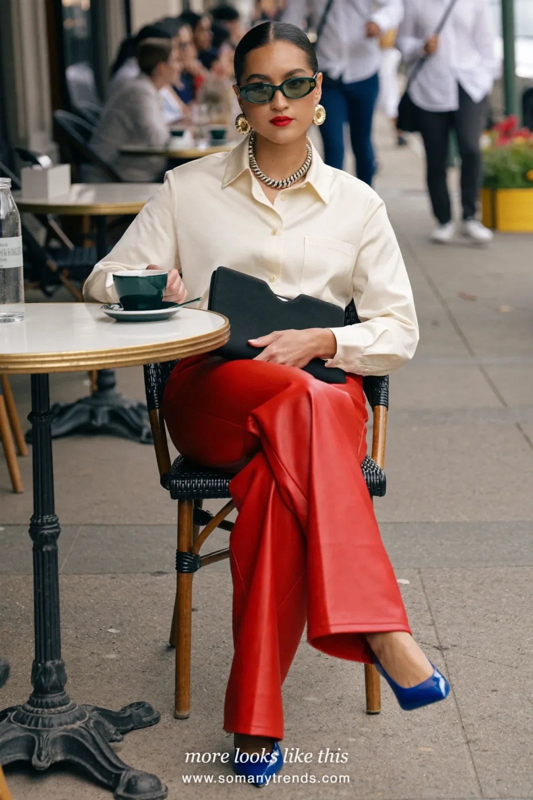 Woman in a cream silk blouse, red soft matte leather straight pants, cobalt blue patent pointed pumps and a black clutch, look 28