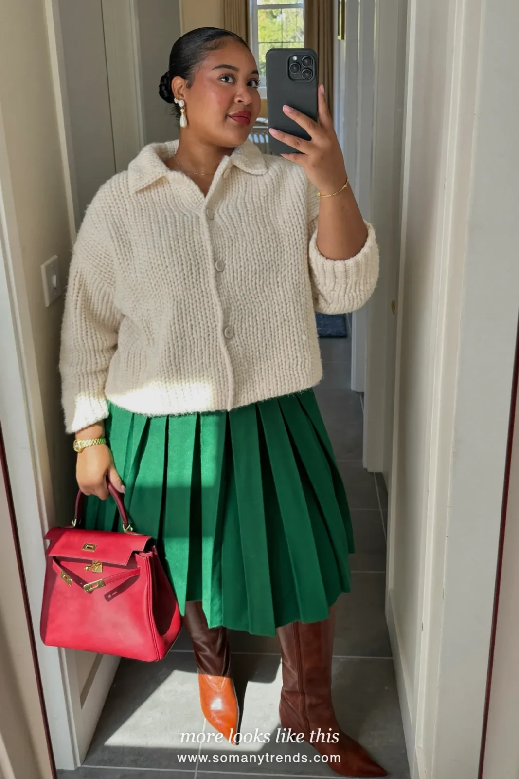Emerald green satin pleated midi skirt, cream chunky knit, brown pointed knee-high boots and cherry red top-handle bag, outfit 12