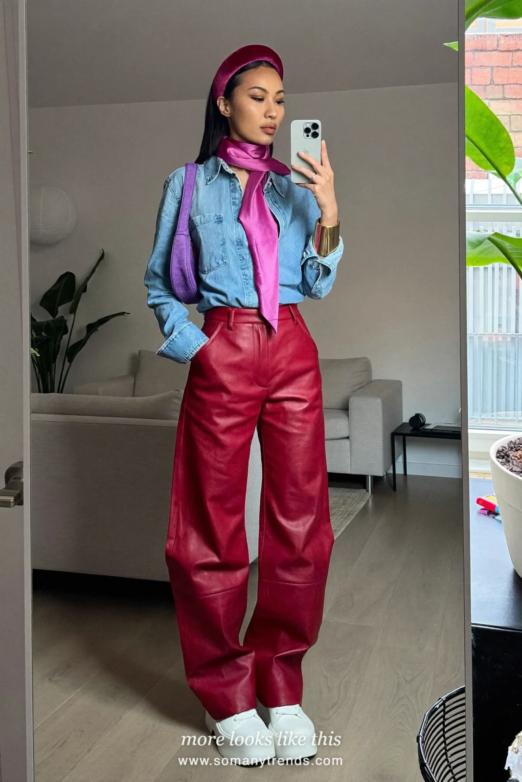 Woman in a light blue denim shirt, pink silk scarf at the neck, red soft matte leather straight pants, white platform sneakers and a violet bag, look 9