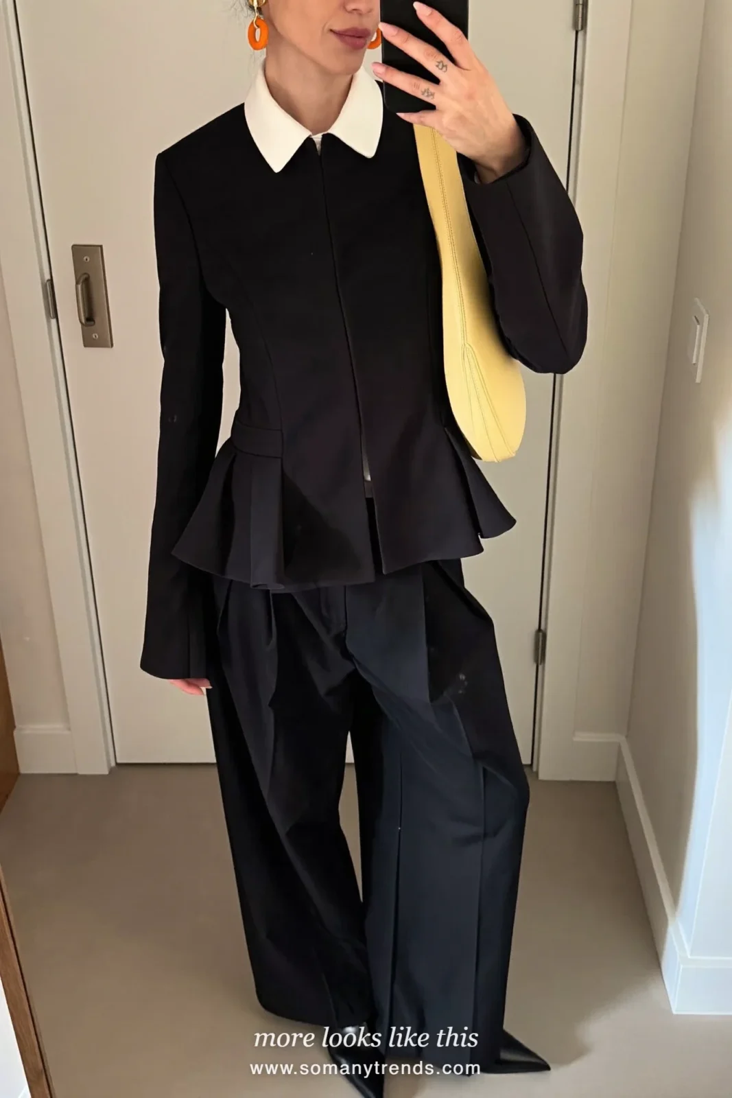 Petite woman in a black peplum jacket with white poplin collar, wide pleated black trousers, black pointed boots and a butter yellow Bottega Veneta Jodie bag, outfit 3