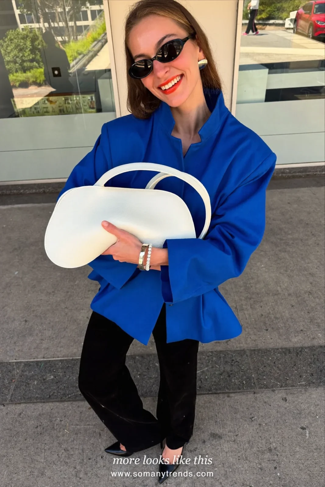 Petite woman in a cobalt blue peplum jacket, black wide pants, black pointed pumps and a white bag, outfit 11