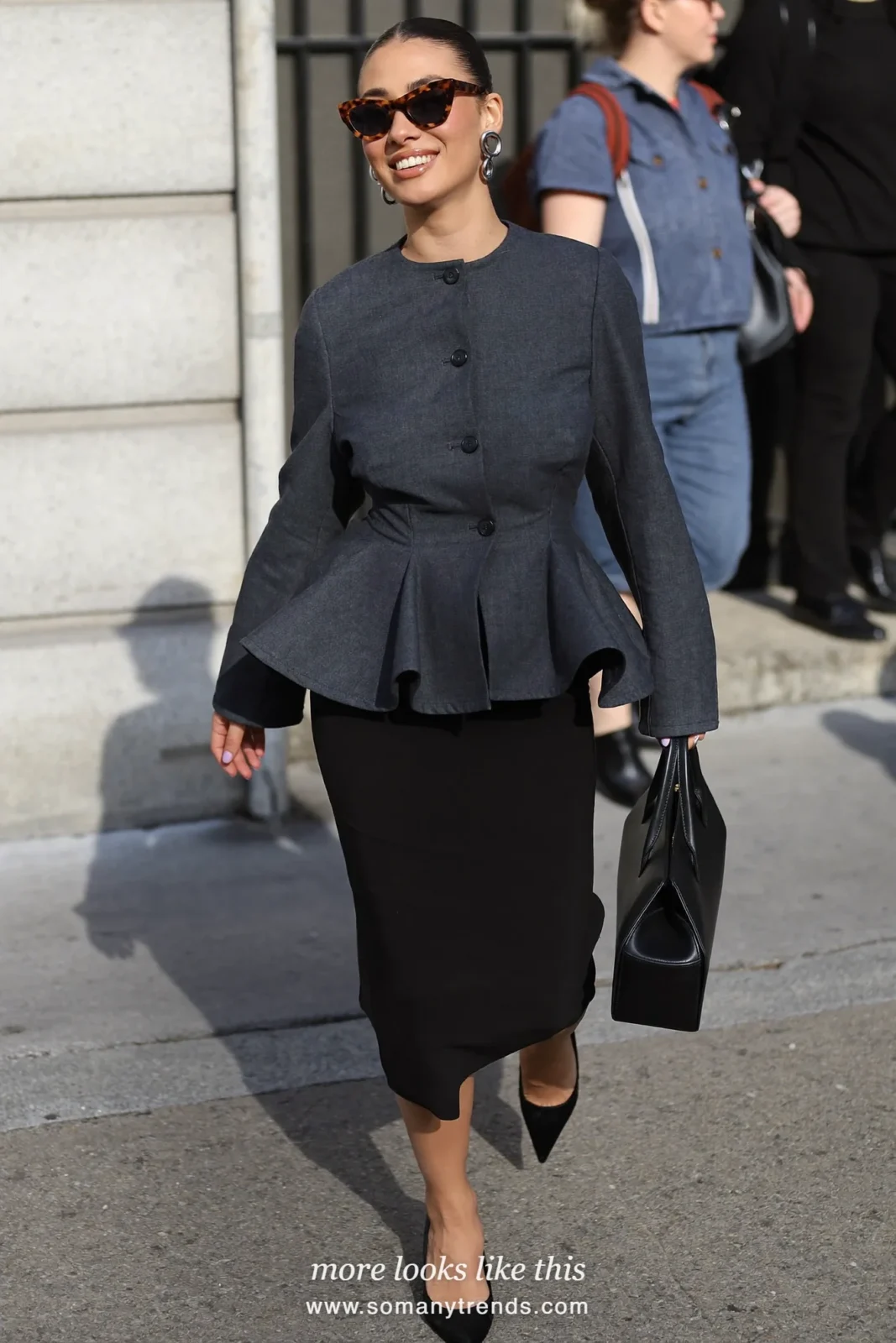 Petite woman in a charcoal peplum jacket, slim black column skirt, black pointed pumps and a black structured bag, outfit 13