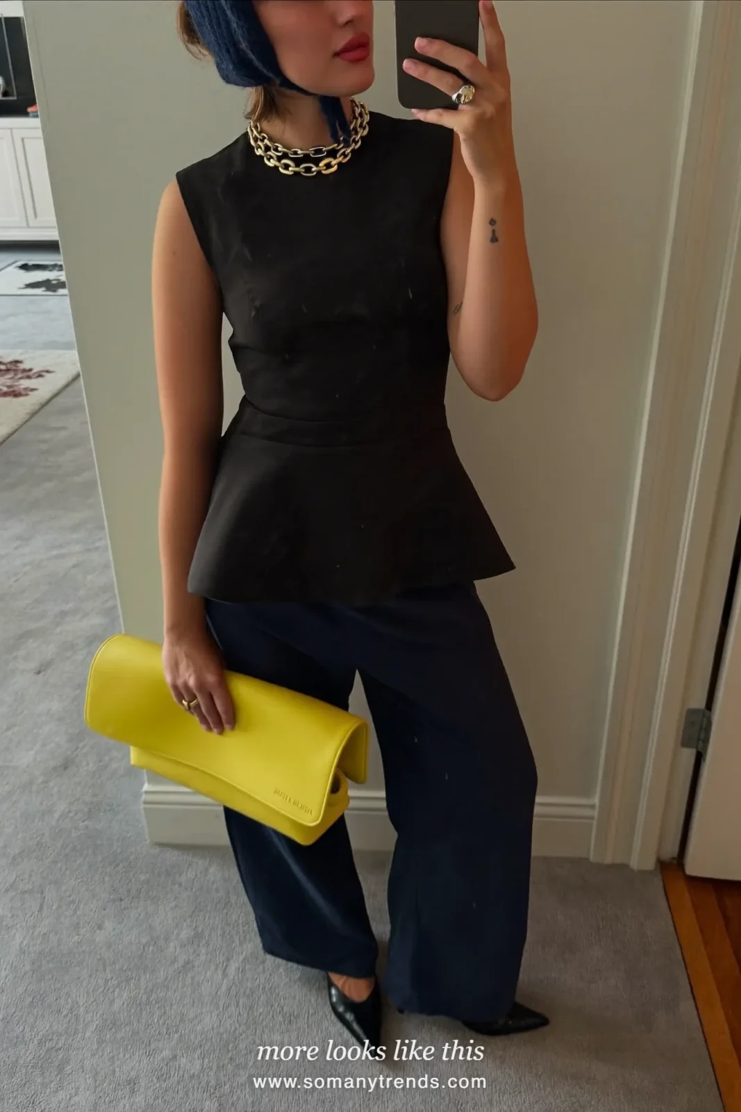 Petite woman in a black peplum top, wide navy pants, black pointed pumps and a butter yellow clutch, outfit 18