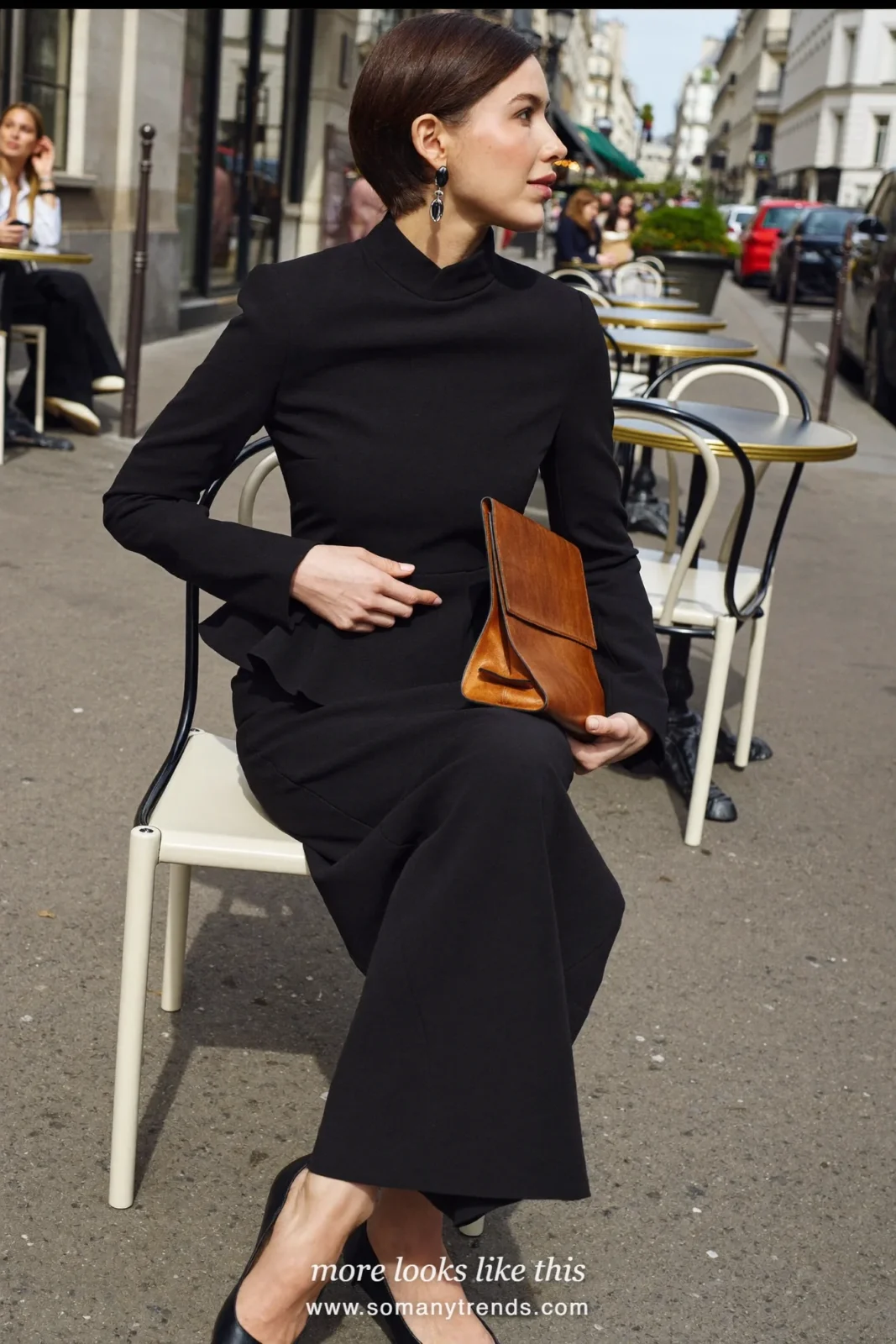 Petite woman in a black peplum jacket, long black column skirt, black pointed pumps and a cognac clutch, outfit 25