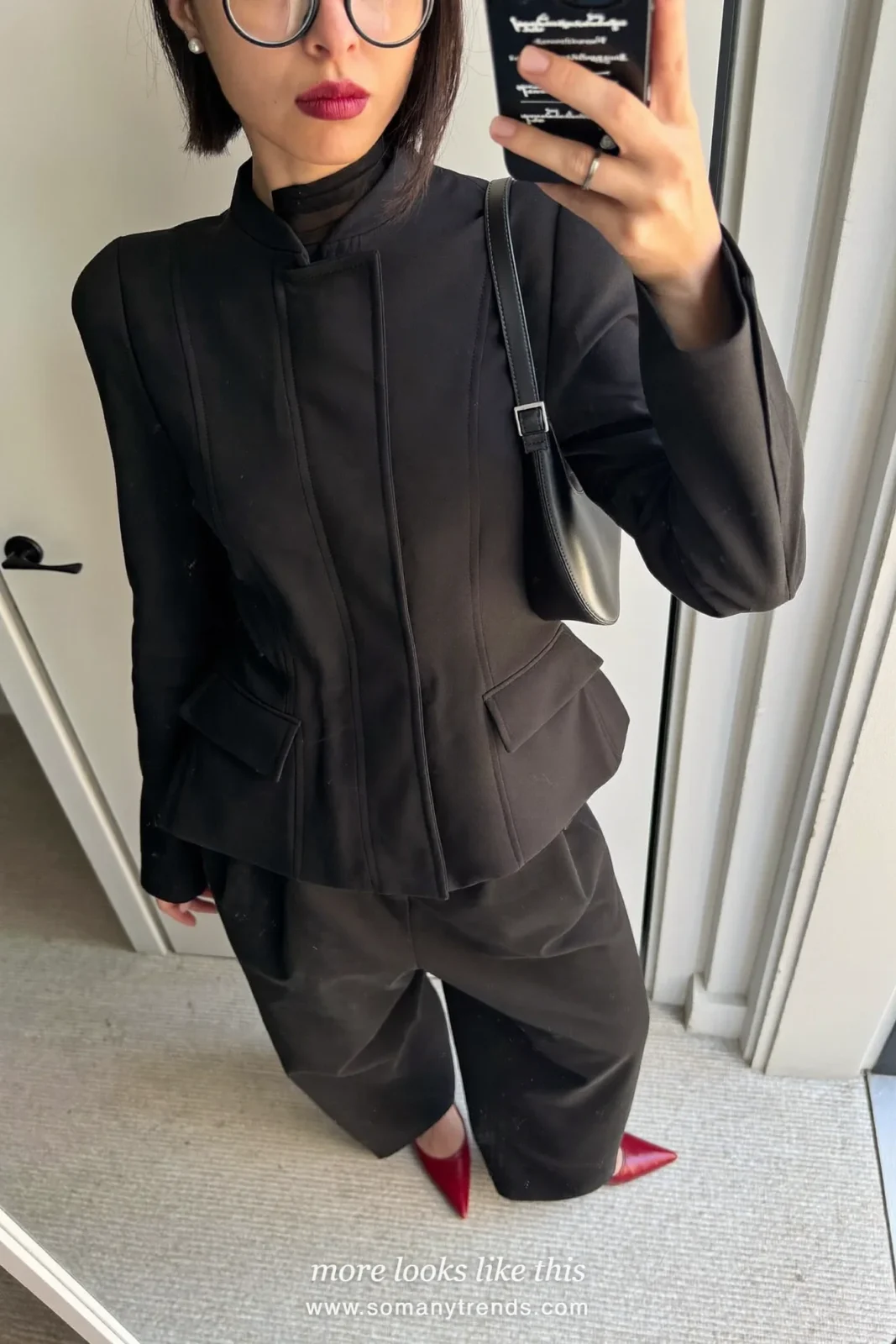 Petite woman in a black peplum jacket, sheer high-neck top, wide black pants, cherry red pointed pumps and a small black bag, outfit 27