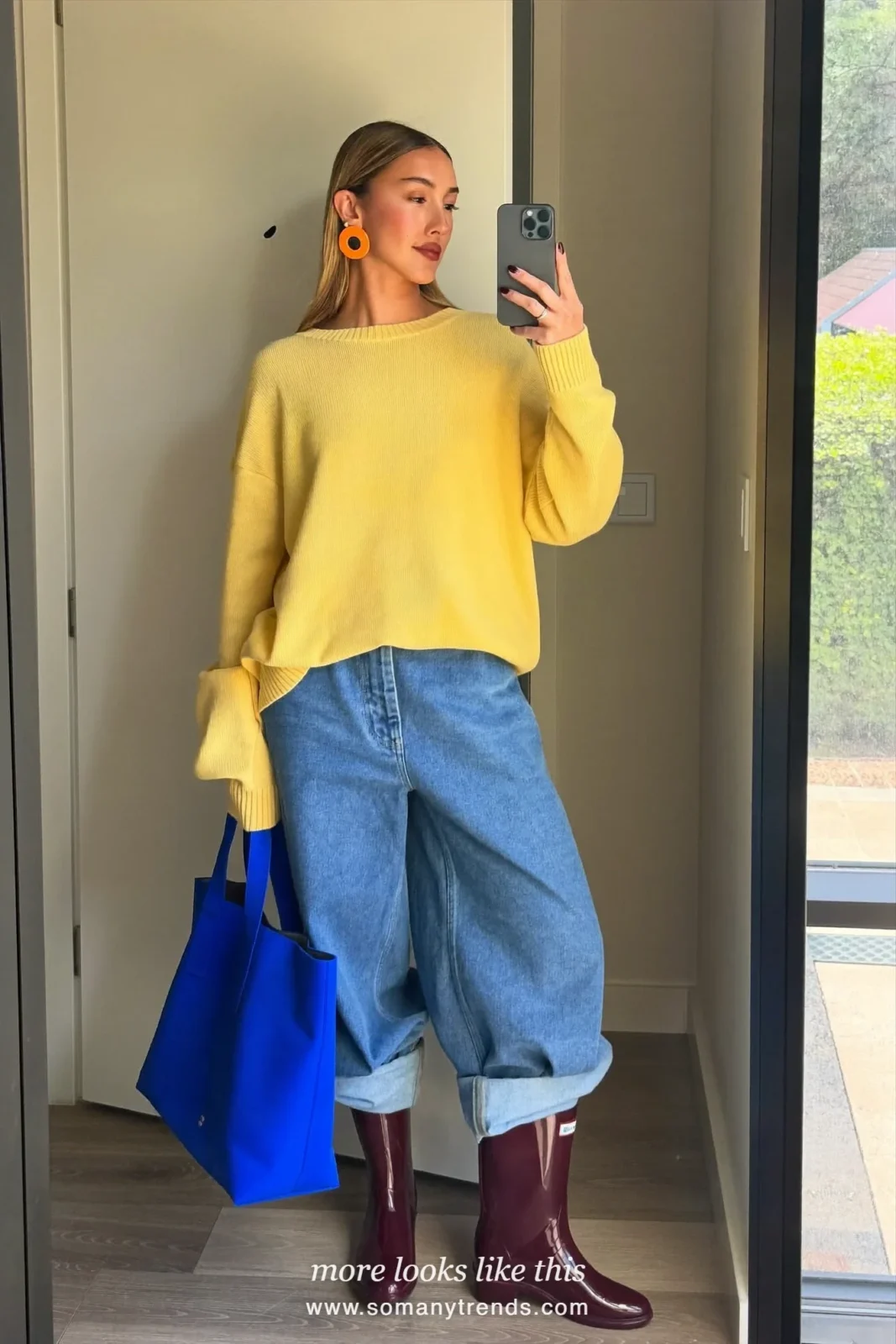 Woman in burgundy glossy short rain boots, straight light jeans cuffed, butter yellow knit and cobalt tote, outfit 3