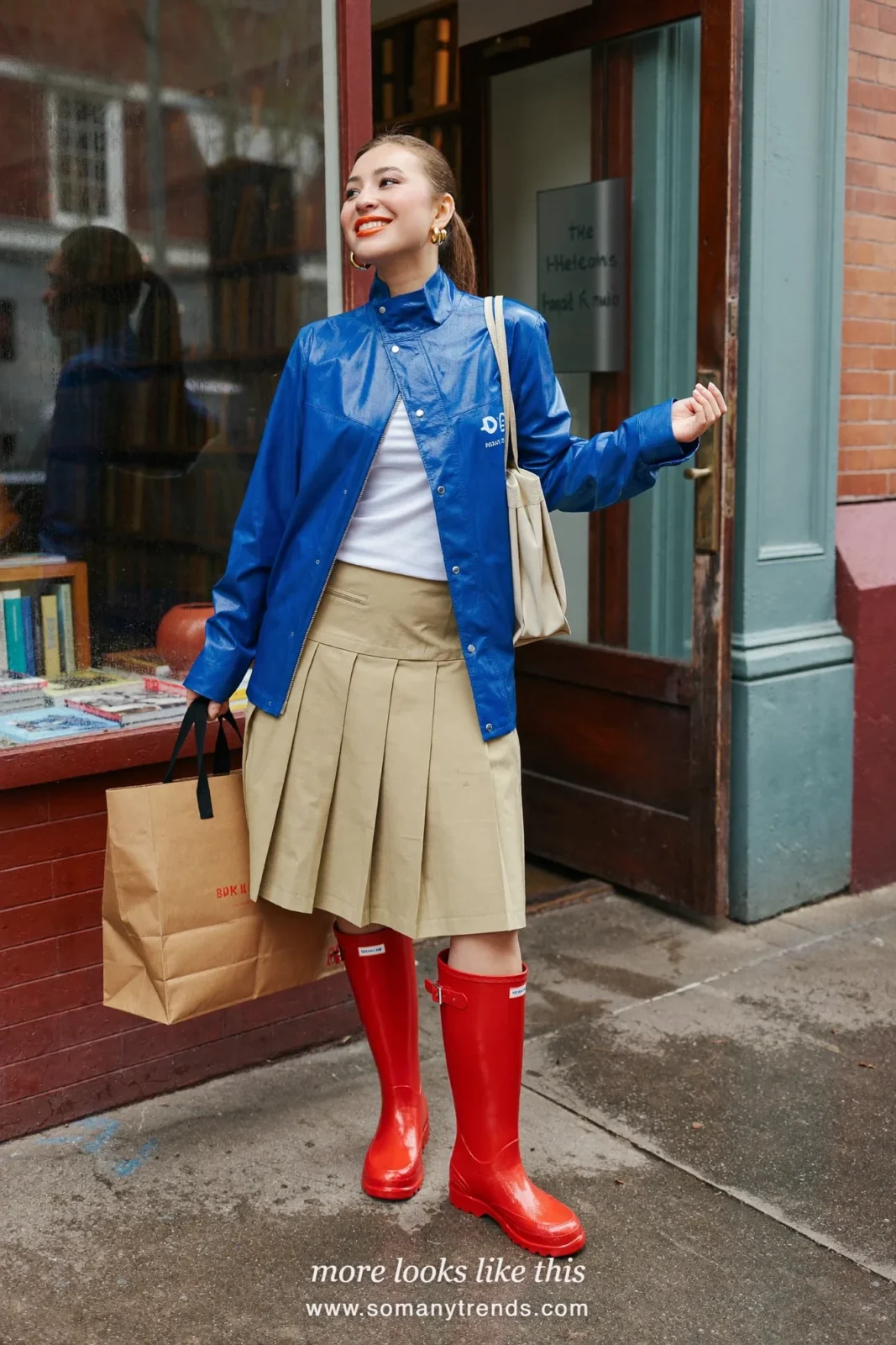 Woman in cherry red glossy tall rain boots, khaki pleated midi skirt, white tee and short cobalt blue rain jacket, outfit 4
