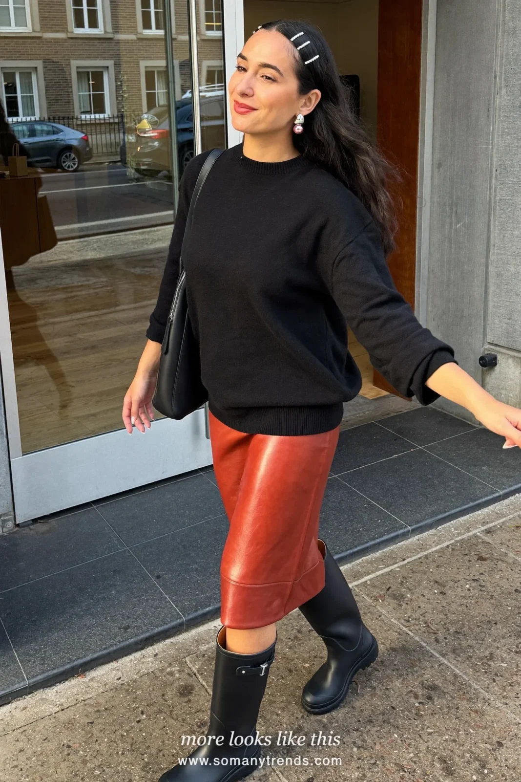 Woman in glossy black tall rubber rain boots, oxblood leather midi skirt and black fine-knit sweater on a city street, outfit 7