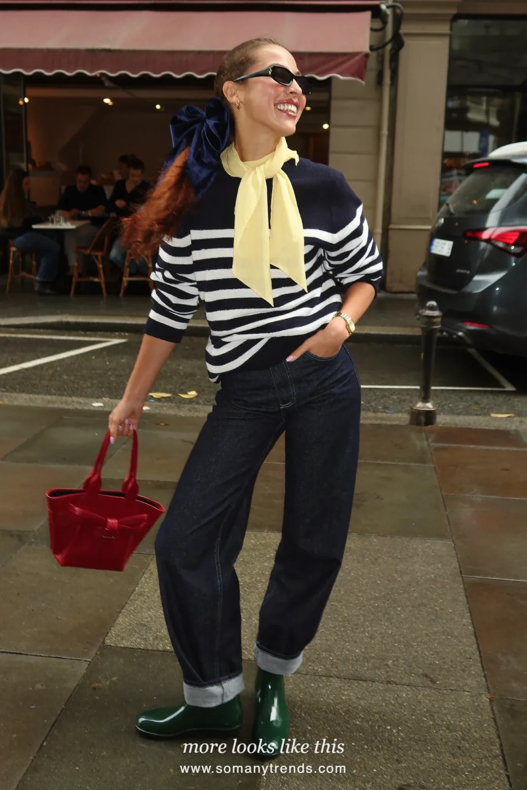 Woman in dark green glossy short rain boots, dark straight jeans cuffed, navy and white striped sweater, red tote and yellow scarf, outfit 10