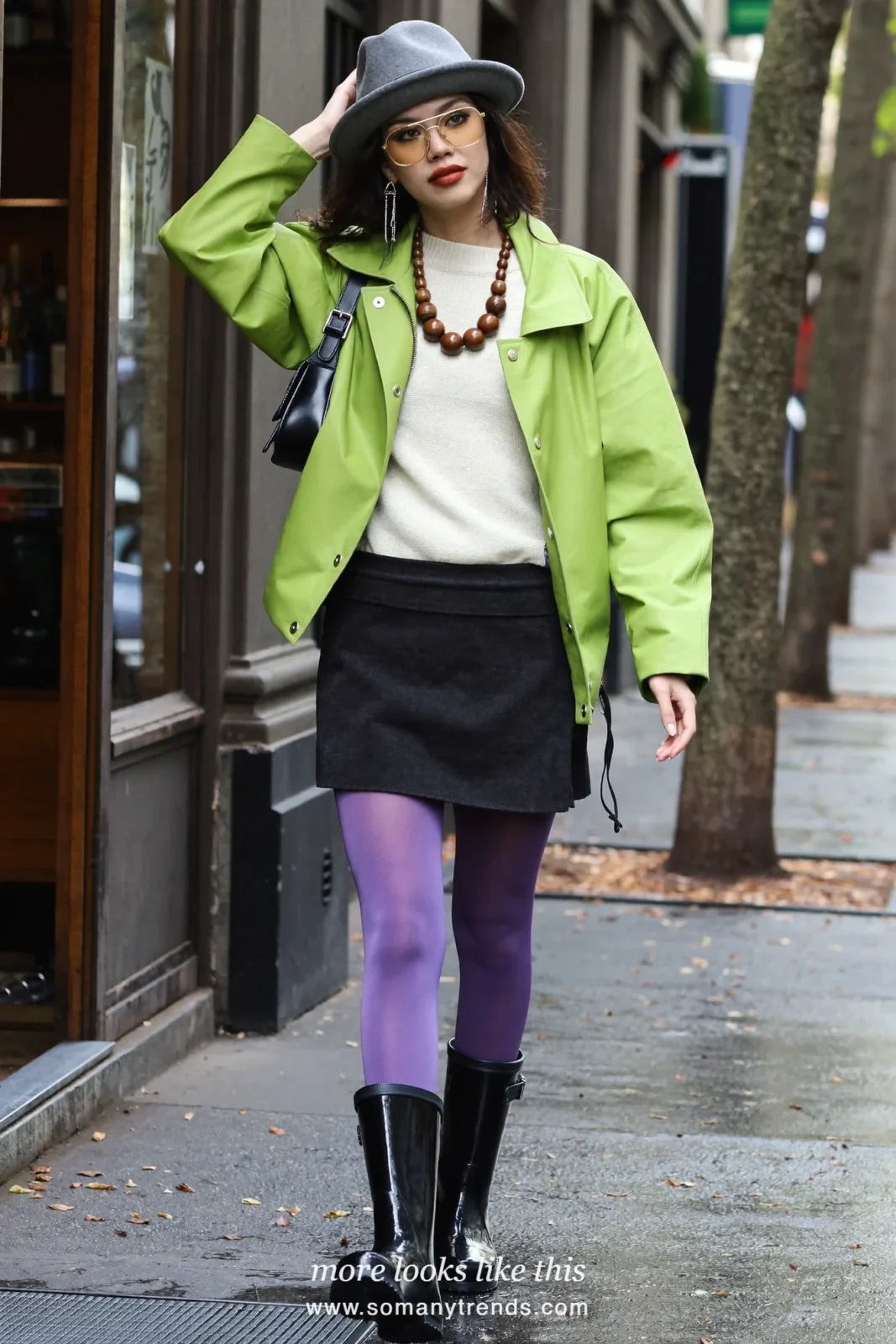 Woman in glossy black short rain boots, violet opaque tights, black mini skirt, cream sweater and short lime green rain jacket, outfit 13