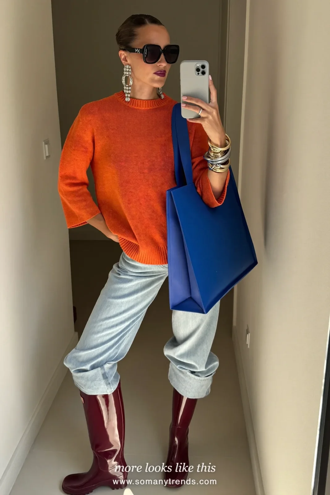 Woman in burgundy glossy tall rain boots, pale blue straight jeans cuffed, orange knit and cobalt tote, outfit 18