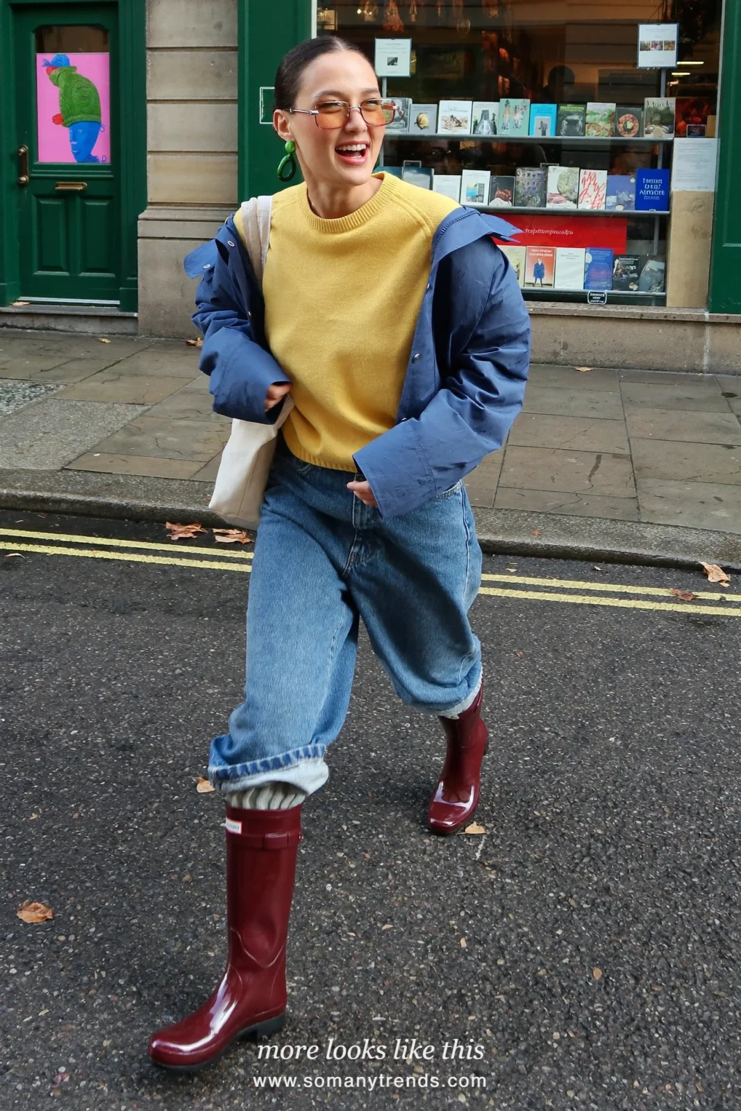 Woman in burgundy glossy tall rain boots, straight mid-wash jeans cuffed, butter yellow knit and short cobalt blue rain jacket, outfit 28