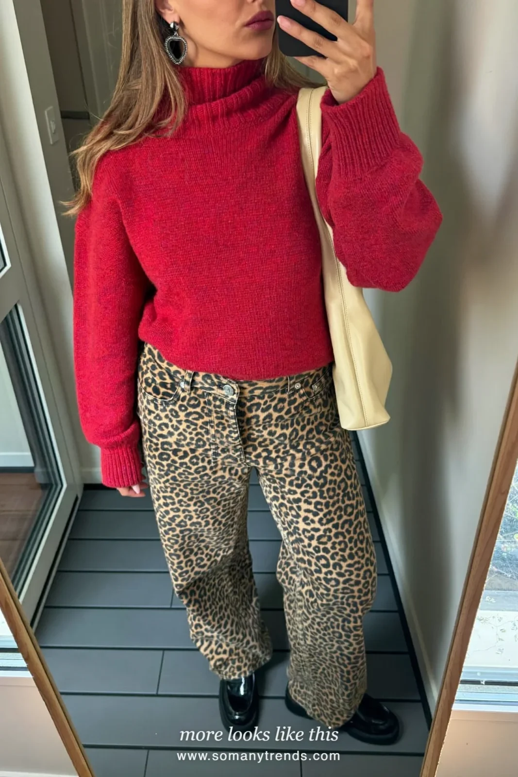 Woman in cherry red knit turtleneck, leopard print straight jeans, black patent loafers and cream bag, outfit 3