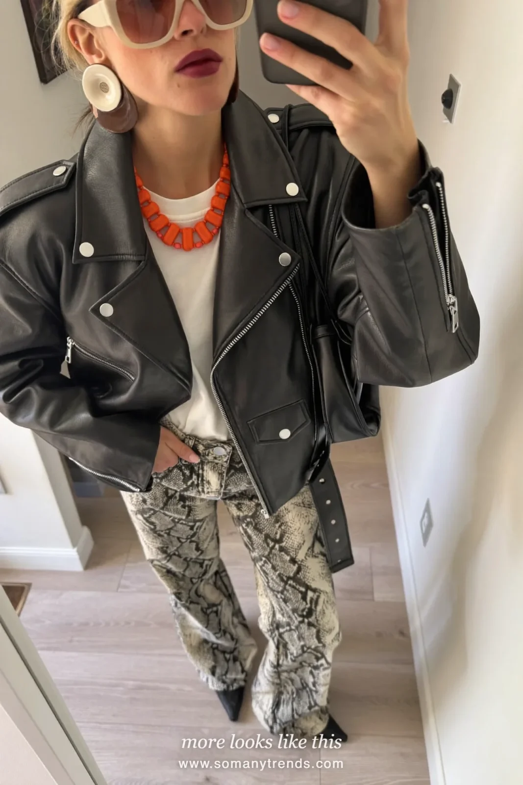 Woman in a black leather jacket, white tee tucked in, black and cream snake print flared pants and black pointed shoes, outfit 12