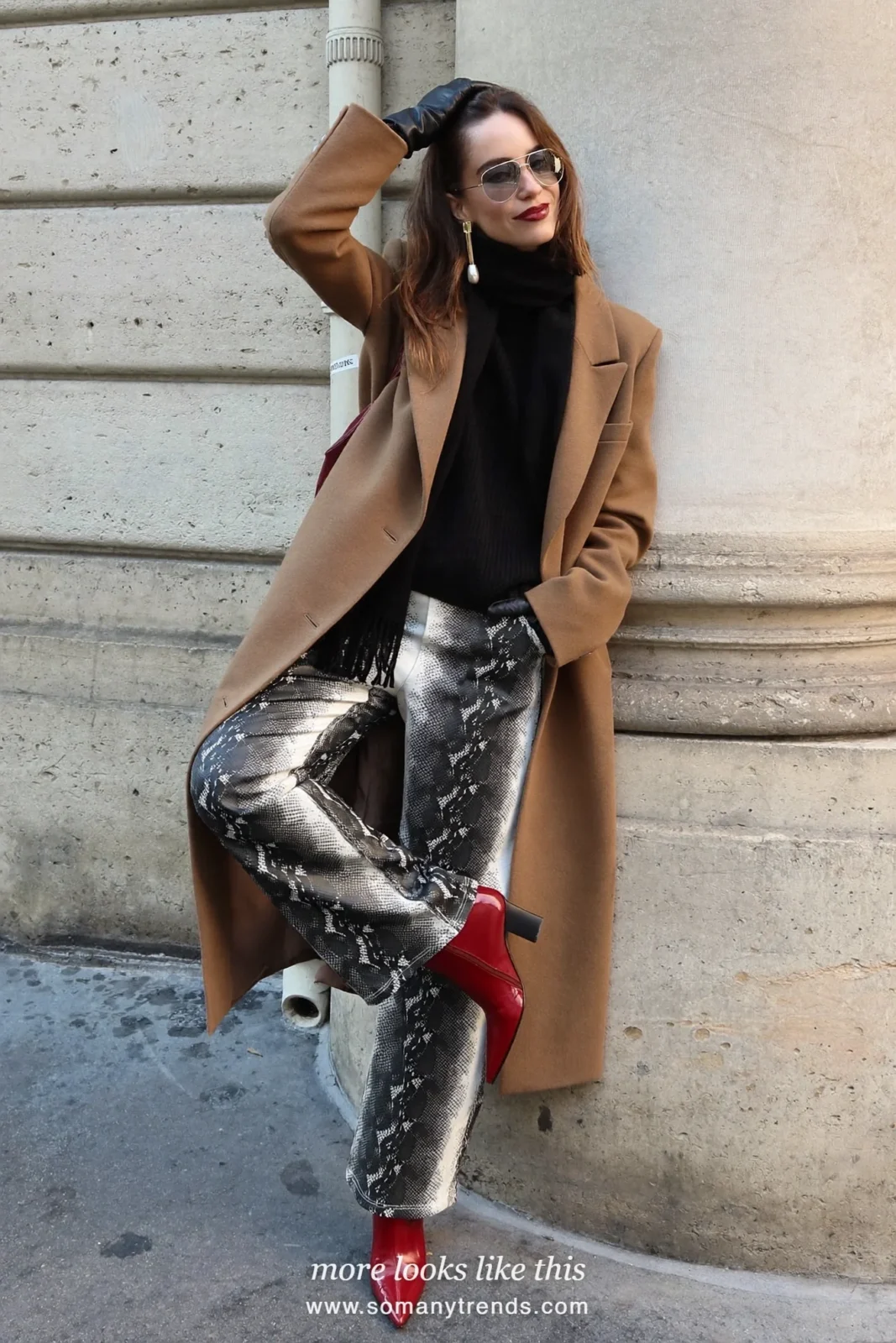 Woman in a camel coat worn open, black knit, black and cream snake print straight pants and cherry red ankle boots, outfit 22