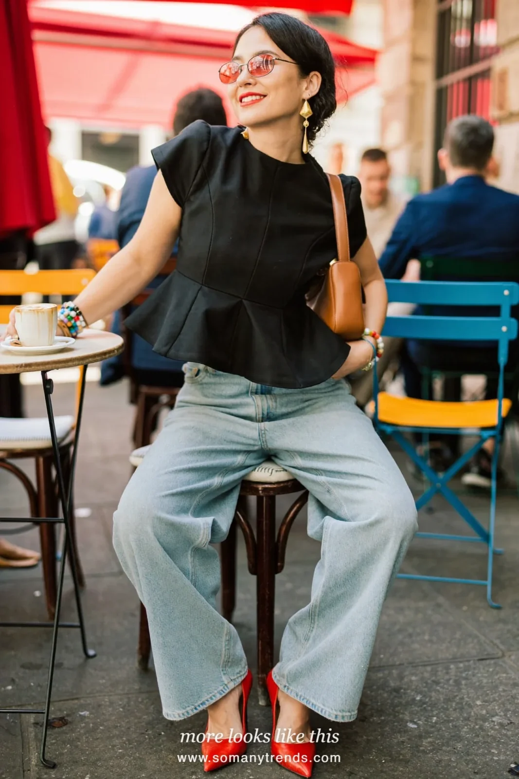 Petite woman in a black structured twill peplum top, wide light wash jeans, red pointed pumps and a tan leather bag, outfit 4