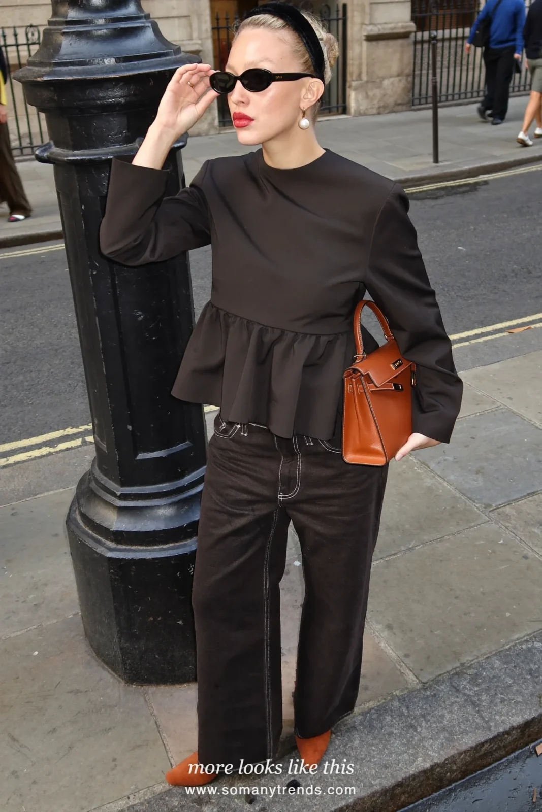 Petite woman in a black twill peplum top, wide dark jeans, cognac pointed boots and a cognac tote, outfit 14