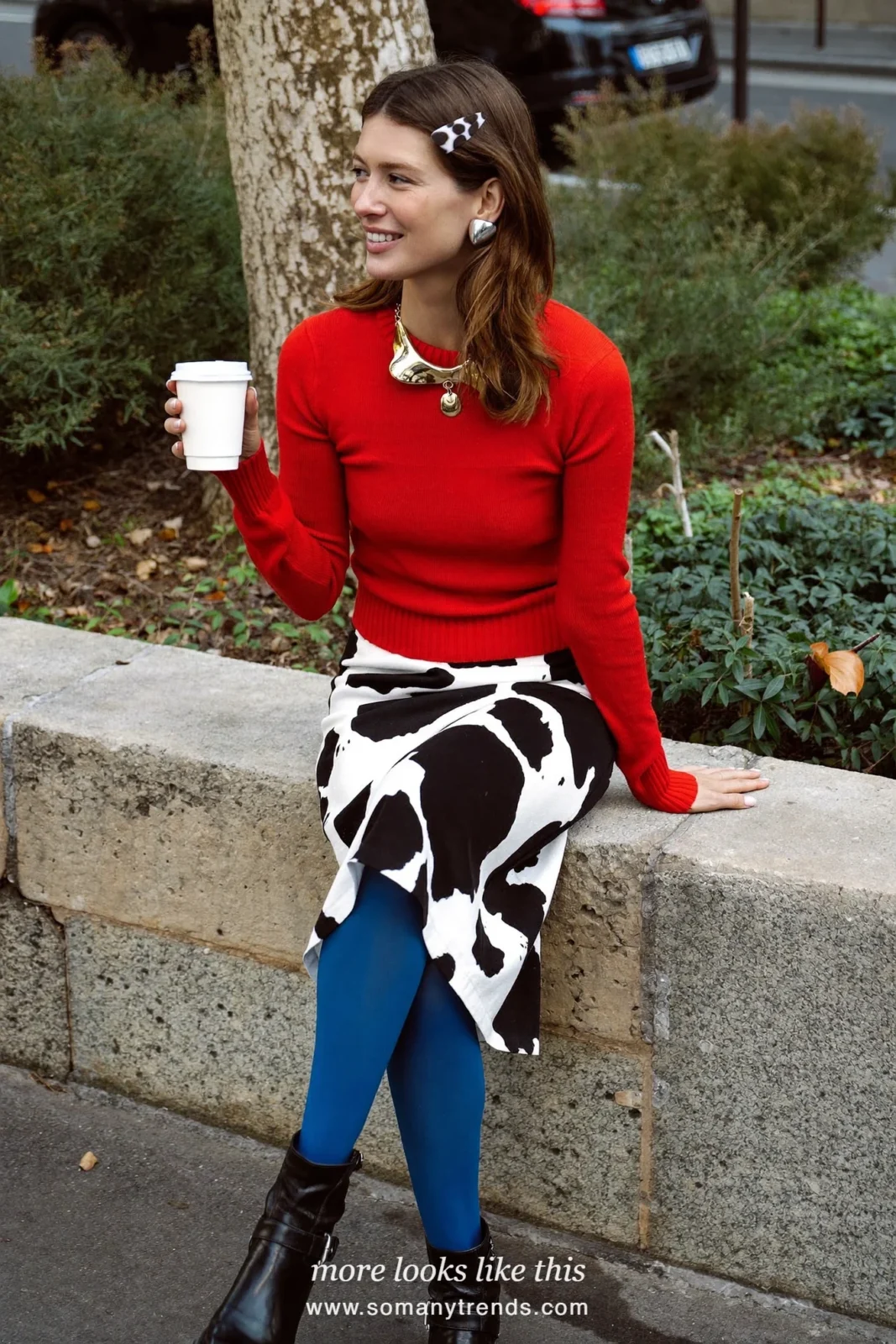 Woman in a black and white cow print midi skirt with a cherry red fitted knit, cobalt blue opaque tights and black ankle boots, outfit 2