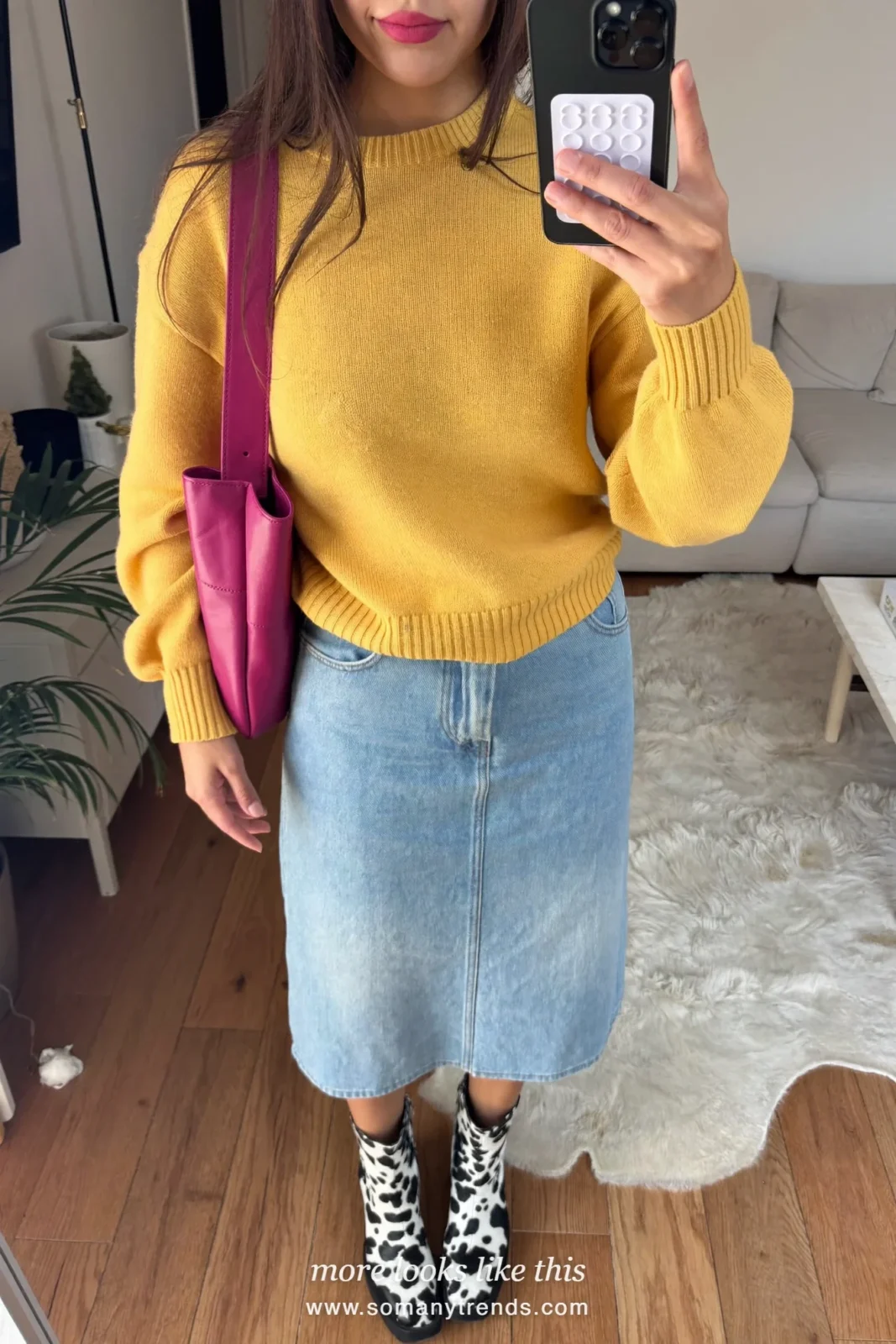 Woman in a pale blue denim midi skirt with a butter yellow knit, black and white cow print ankle boots, fuchsia bag and tan trench coat worn open, outfit 9