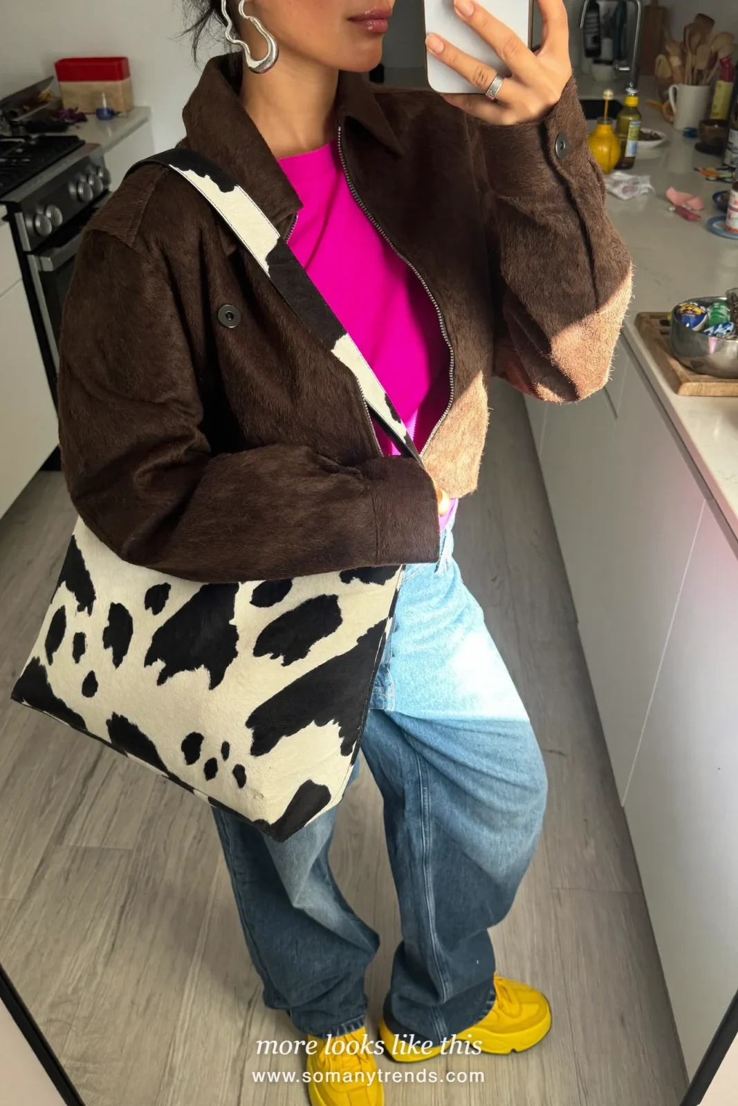 Woman in a chocolate brown suede shirt-jacket over a hot pink tee with wide-leg jeans, yellow platform sneakers and a black and white cow print bucket bag, outfit 12