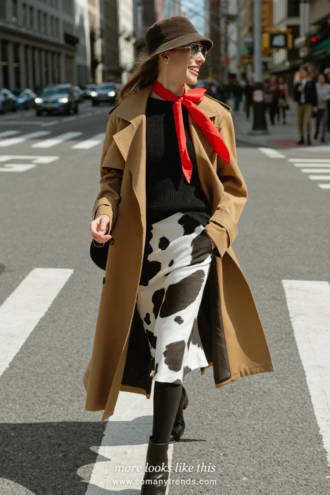 Woman in a black and white cow print midi skirt with a black knit sweater, camel coat worn open and black ankle boots, outfit 13