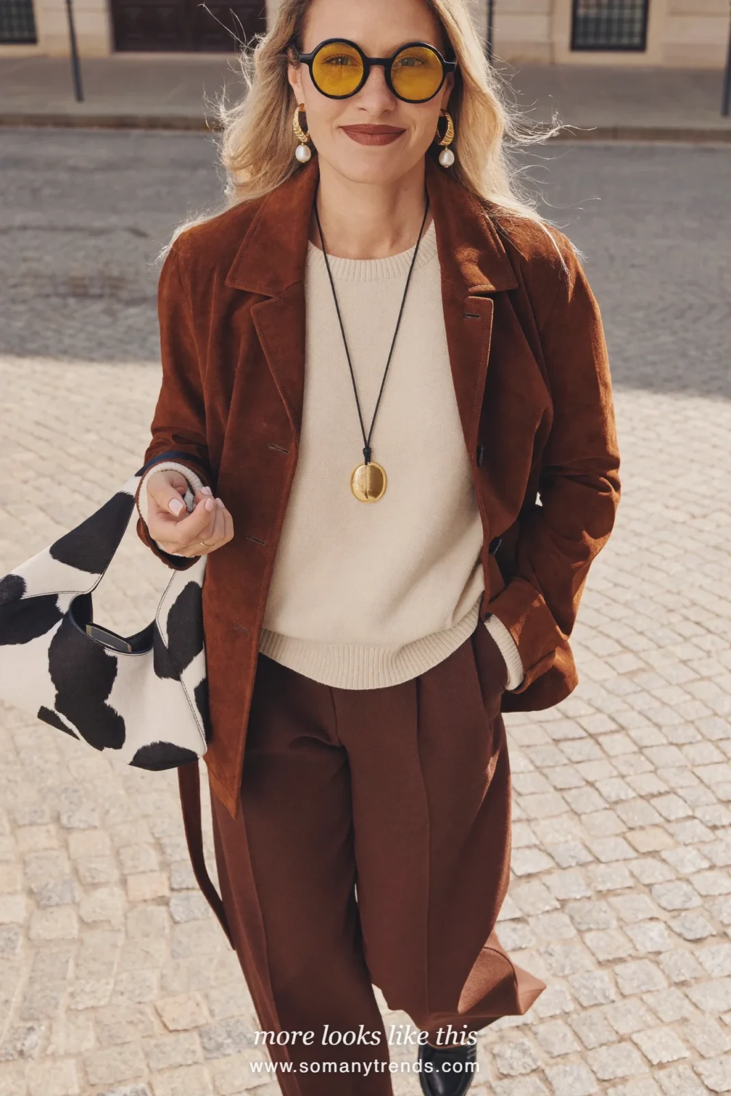 Woman with a black and white cow print shoulder bag, brown suede jacket, cream knit and chocolate brown wide pants, outfit 14