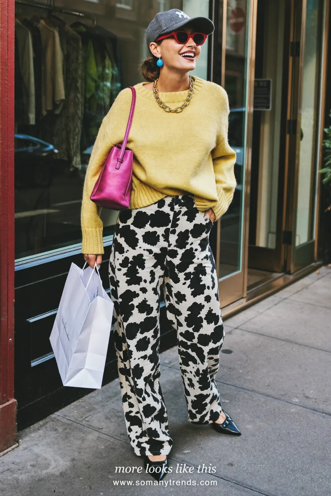 Woman in black and white cow print wide-leg pants with a butter yellow knit, black pointed flats and a fuchsia bag, outfit 17