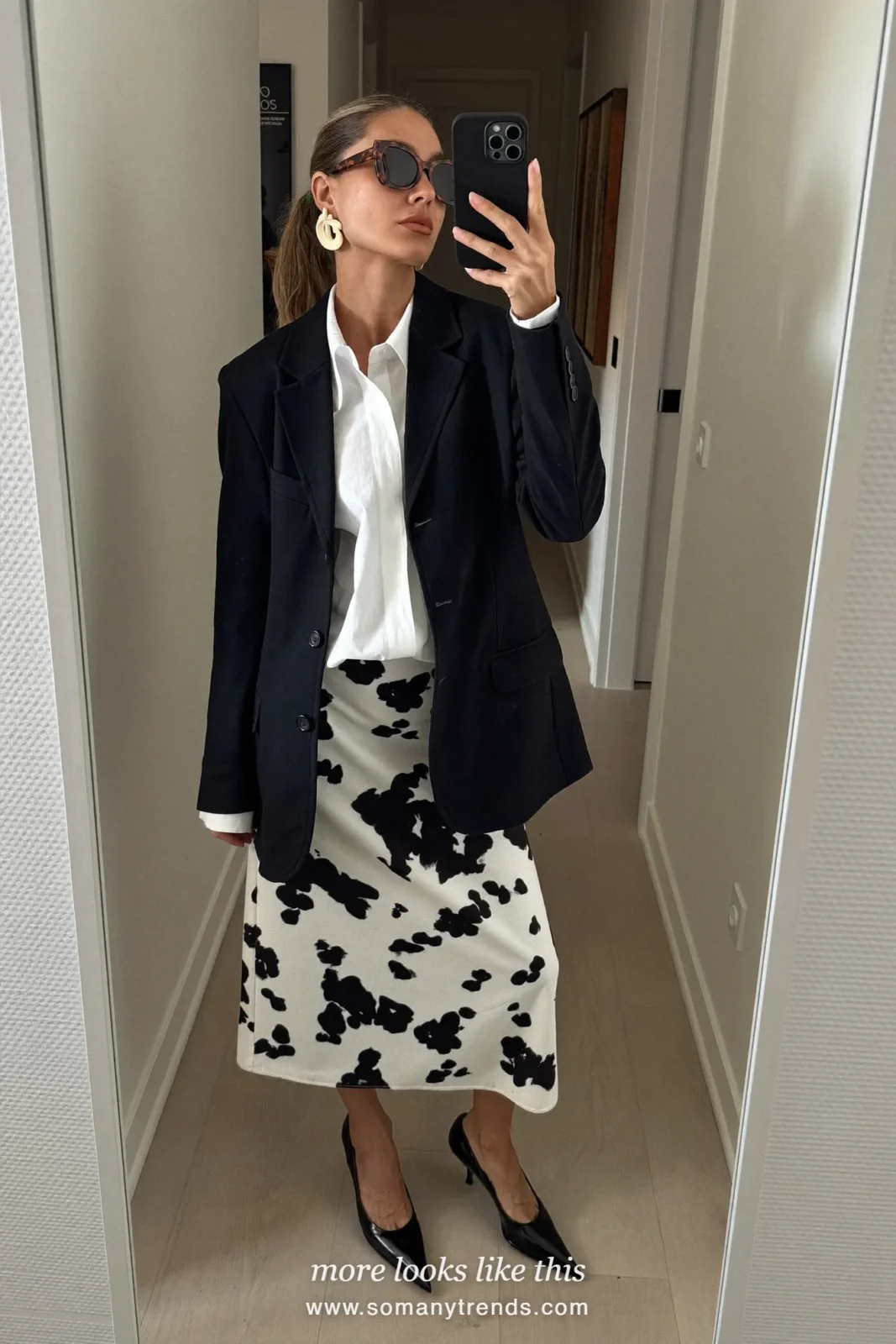 Woman in a black and white cow print midi skirt with a white blouse, black blazer, black pointed pumps and a black clutch, outfit 21