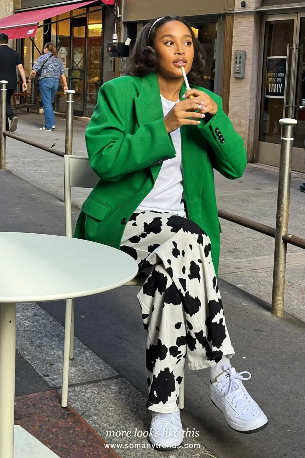 Woman in black and white cow print straight pants with an emerald green relaxed blazer, white tee and white sneakers, outfit 23