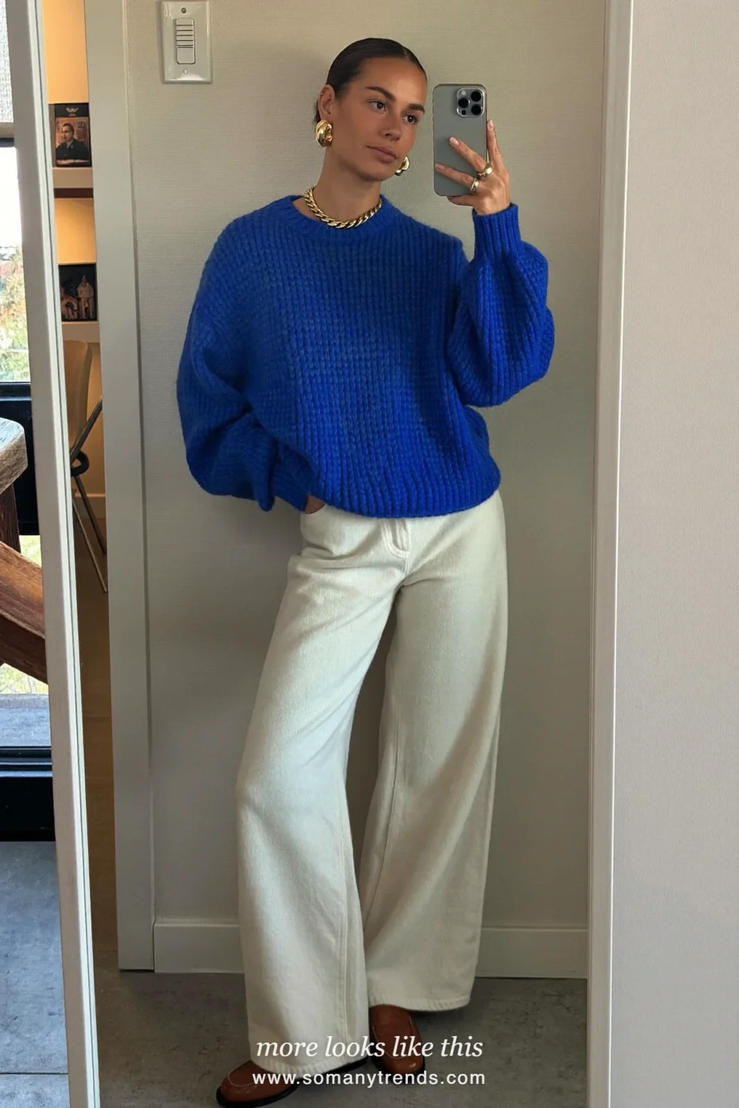 Woman in a cobalt blue chunky sweater, cream wide-leg pants, gold chain necklace, gold hoops and tan loafers, outfit 9
