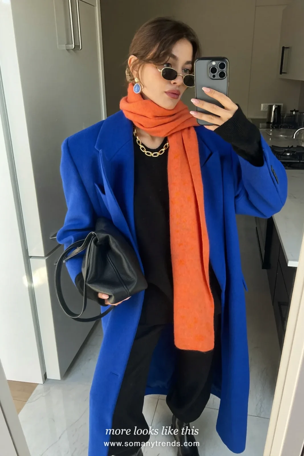 Woman in a long cobalt blue coat with a tangerine orange scarf, black knit, black pants and black boots, outfit 21