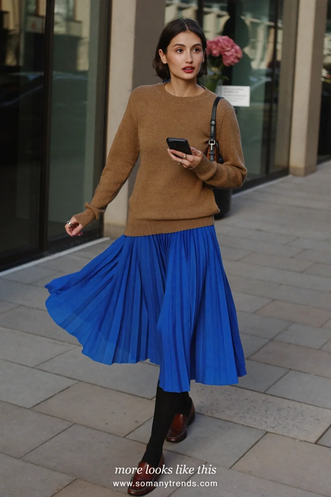 Woman in a camel knit sweater, cobalt blue pleated midi skirt, sheer black tights and brown loafers, outfit 25