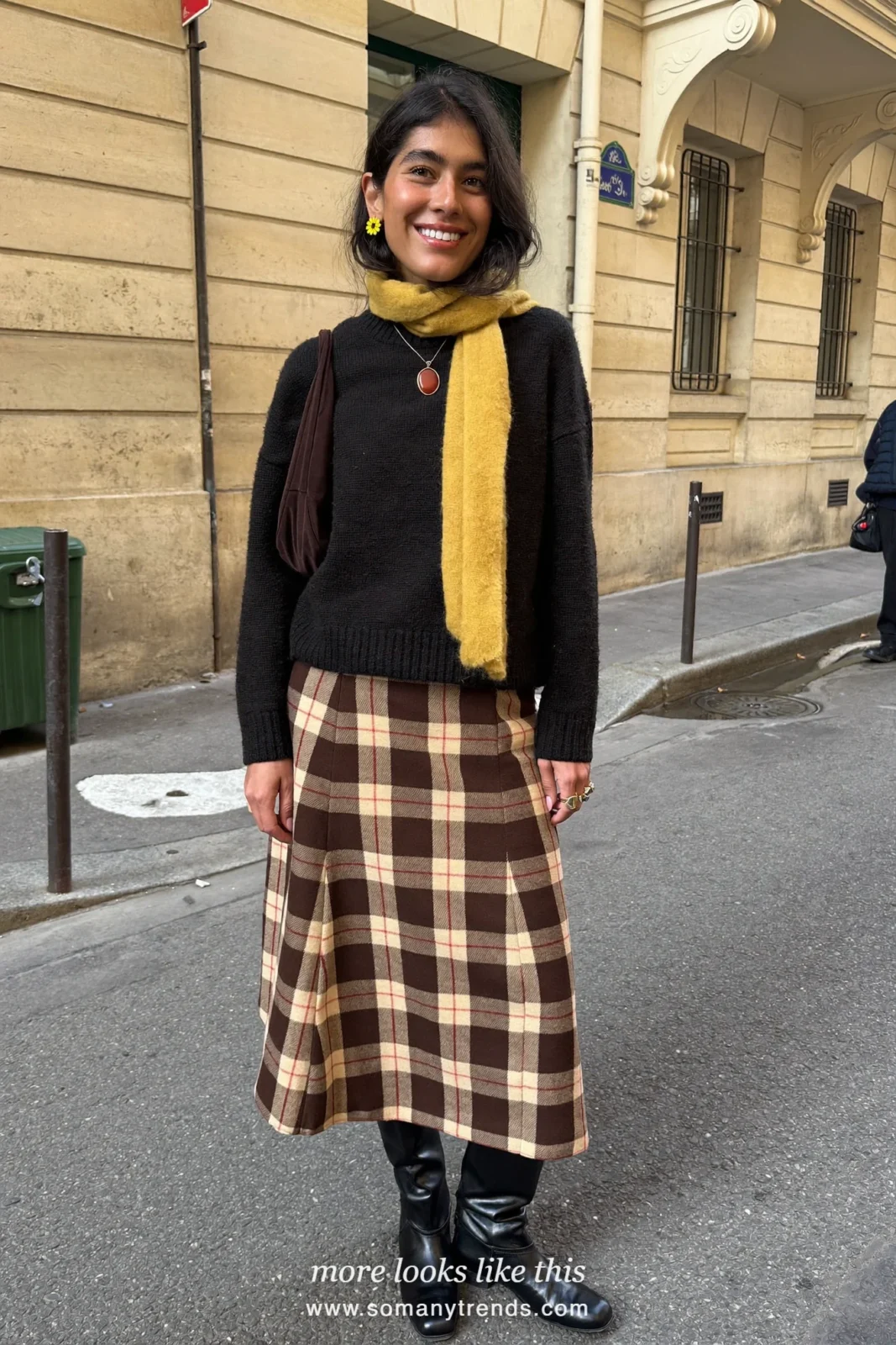 Woman in a black crewneck sweater, brown and cream plaid midi skirt, black knee boots and a butter yellow scarf, look 4