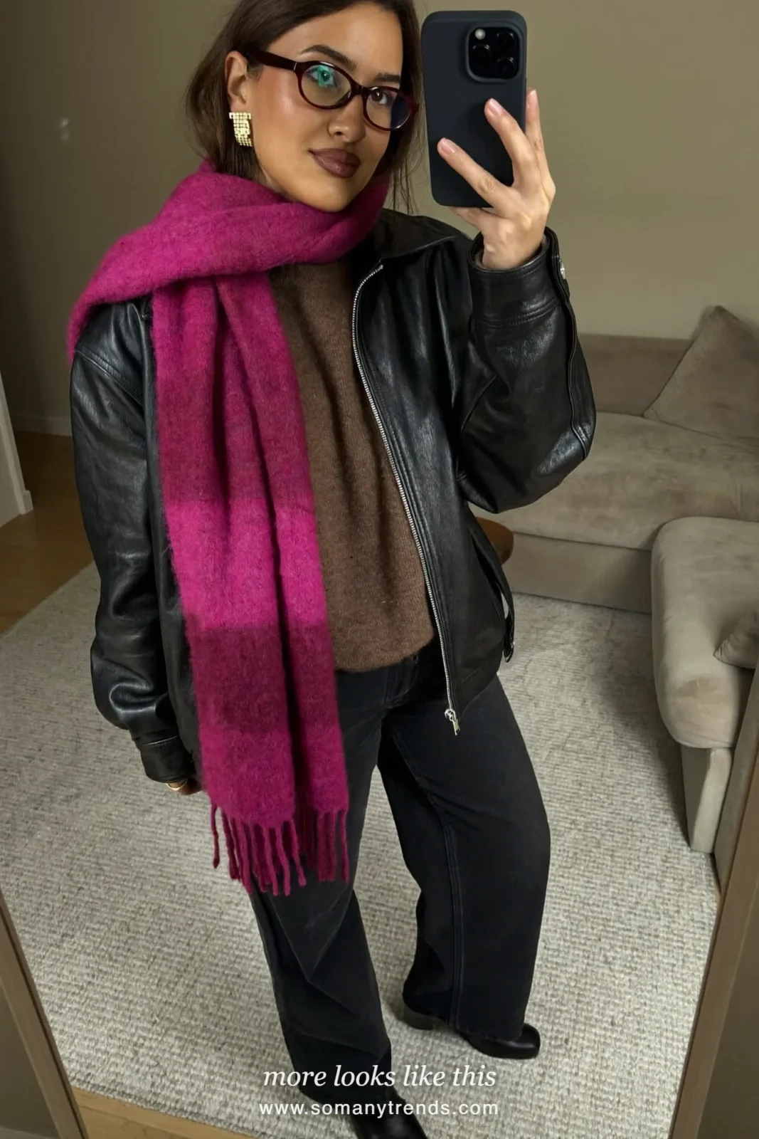 Woman in a black glossy leather jacket over a brown cashmere sweater with black jeans, black boots and a fuchsia scarf, look 9