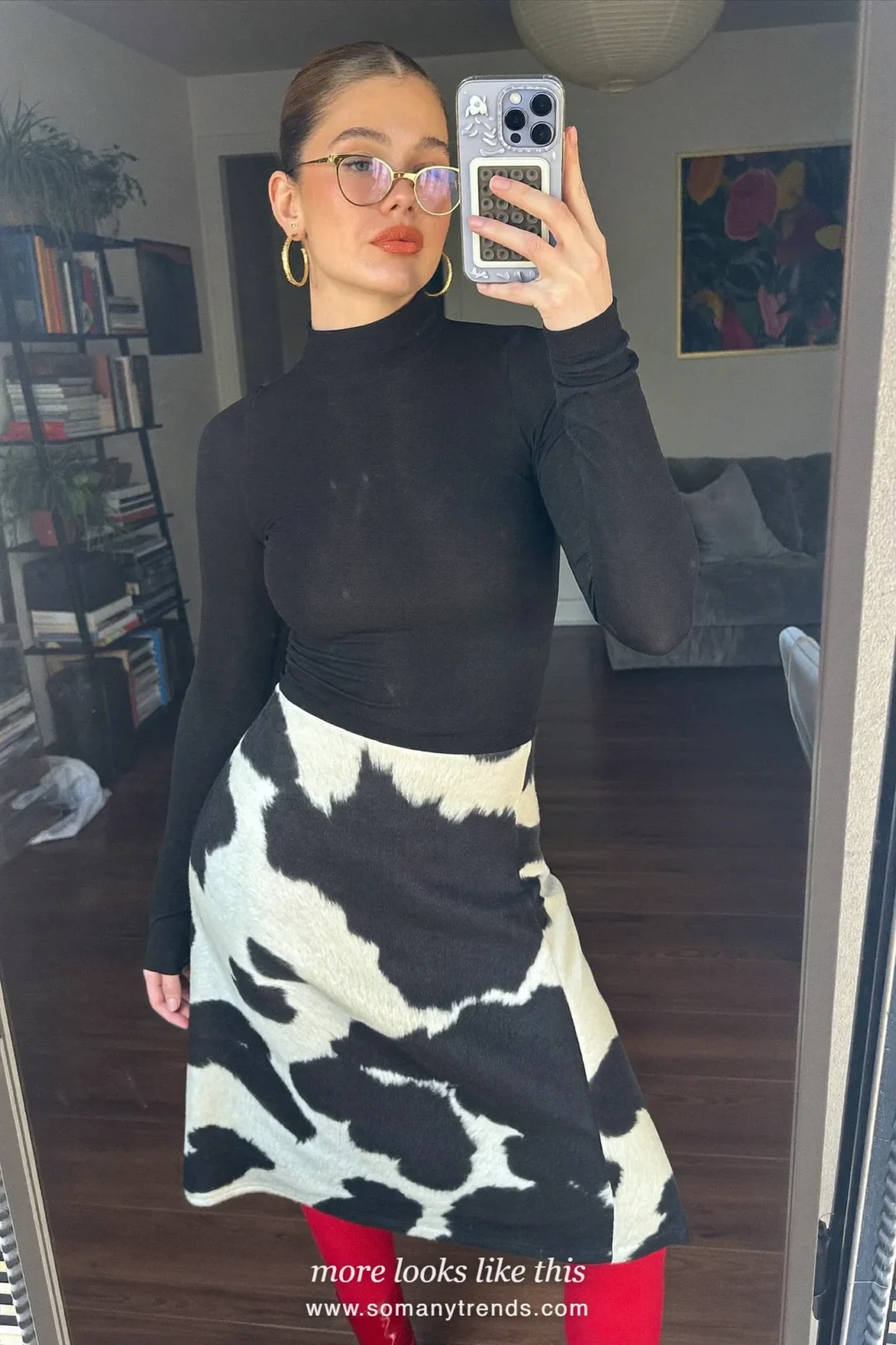 Woman in a black fitted turtleneck tucked into a black and white cow print midi skirt with cherry red patent boots and a black clutch, outfit 18