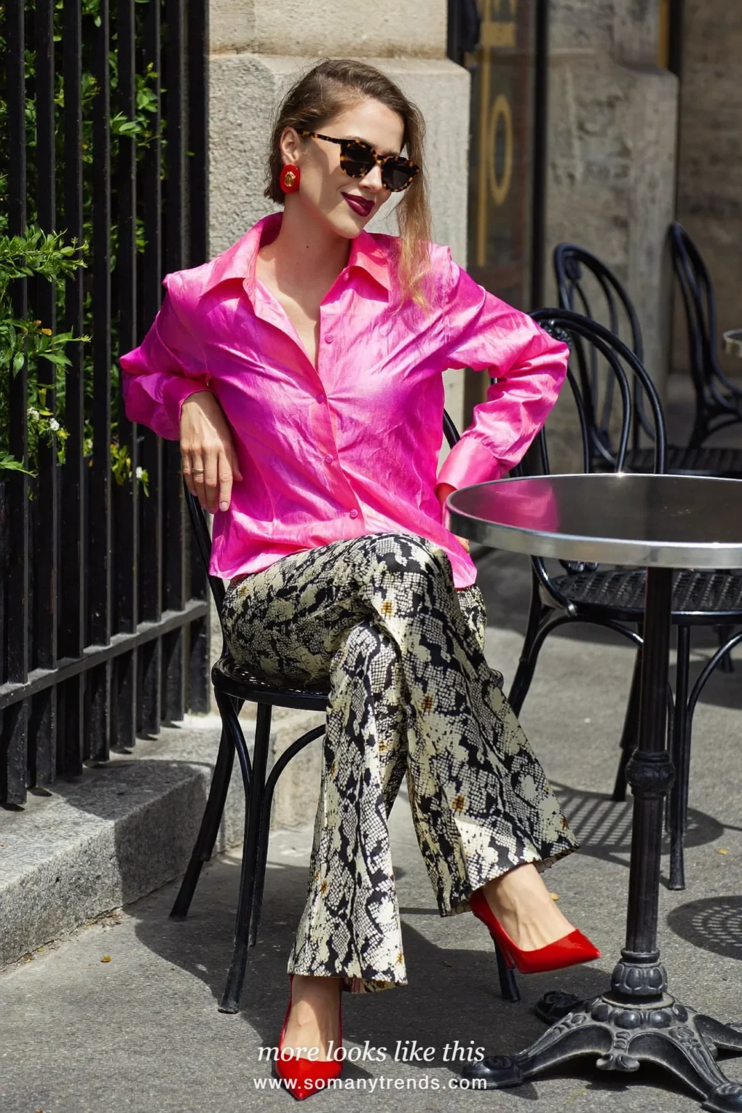 Woman in a hot pink satin shirt, black and cream snake print flared pants, red patent pointed pumps and a black bag, outfit 1