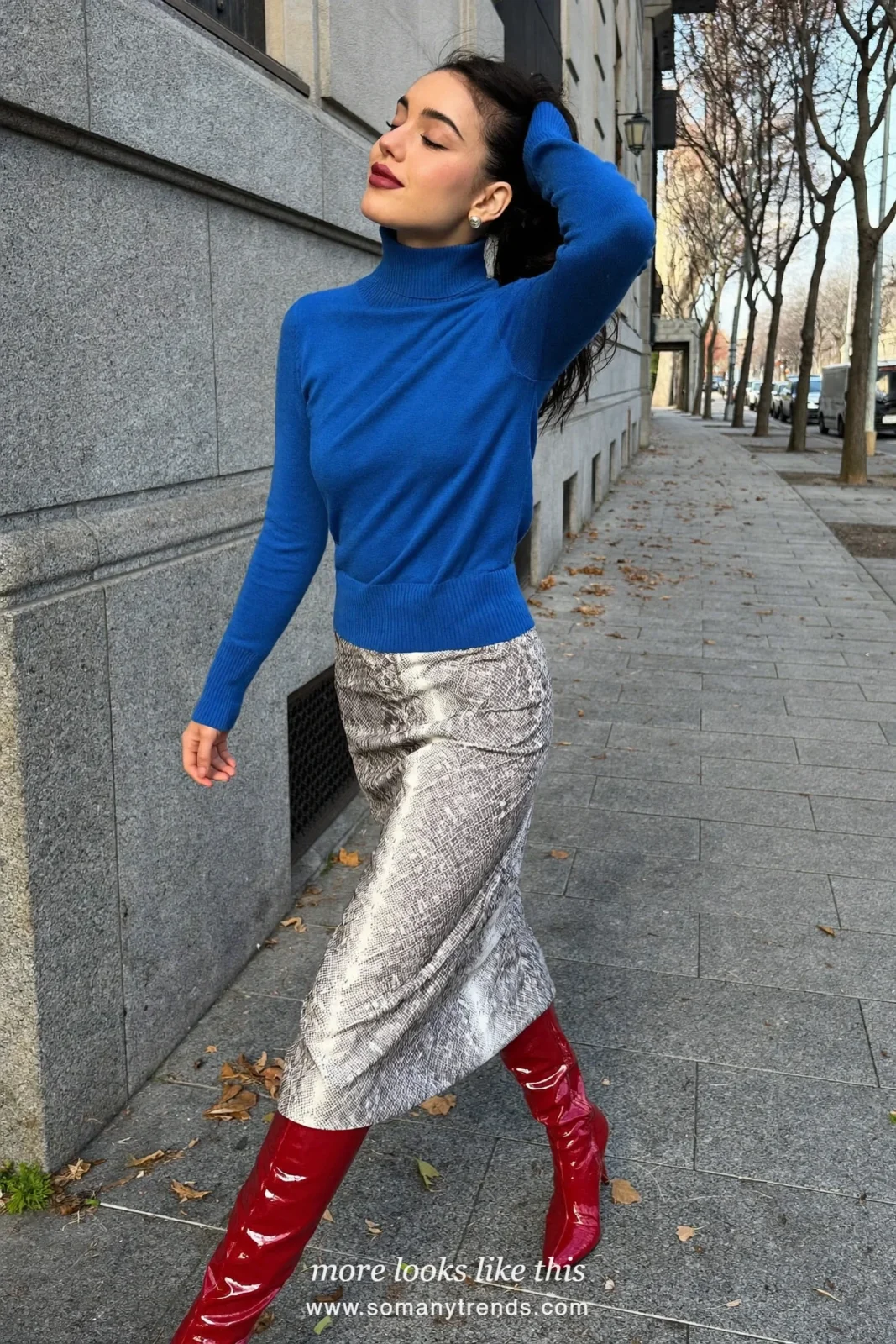 Woman in a cobalt blue turtleneck, gray and white snake print midi skirt, cherry red patent knee boots and a black bag, outfit 2