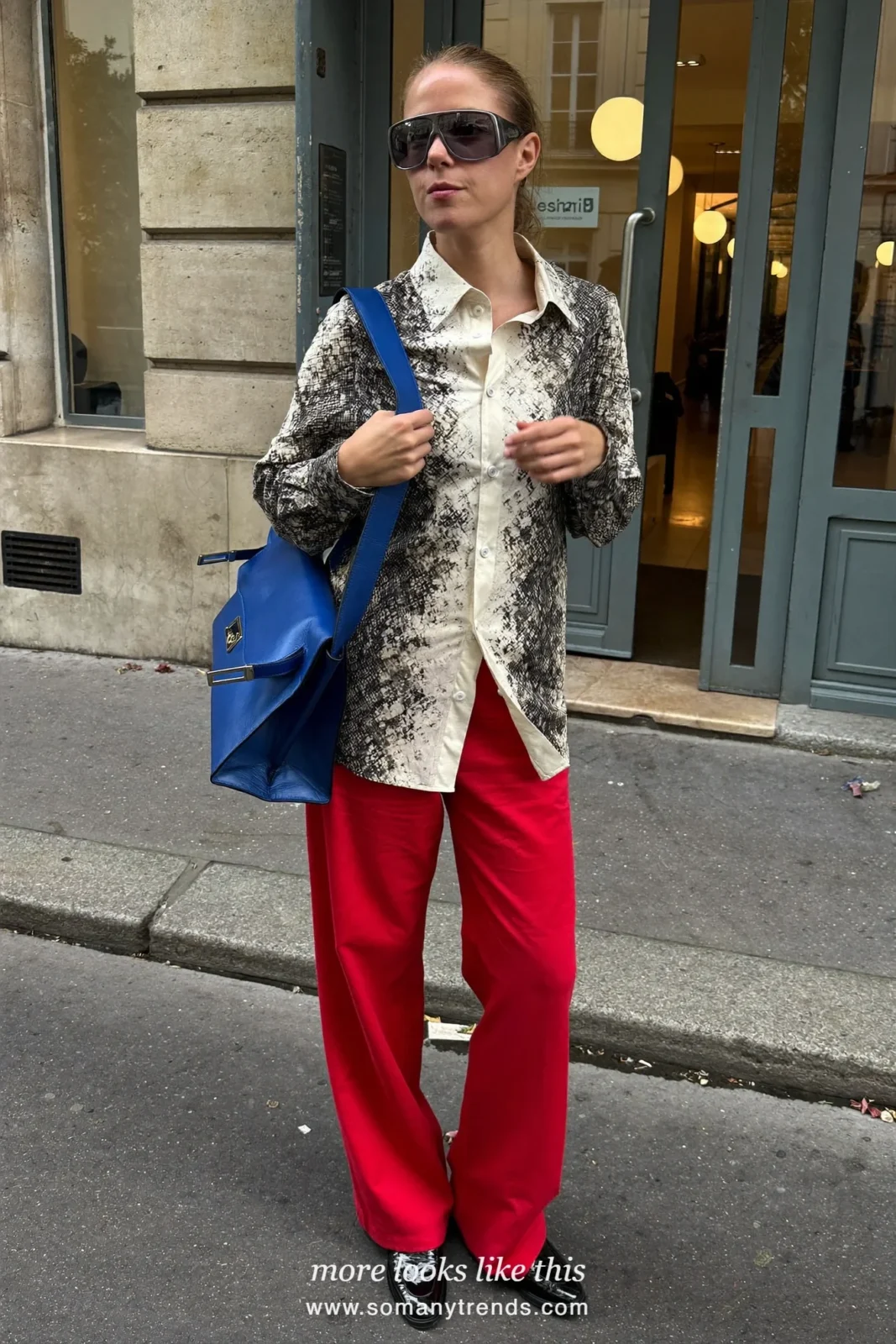 Woman in a black and cream snake print shirt, cherry red wide trousers, black patent loafers and a cobalt blue bag, outfit 5