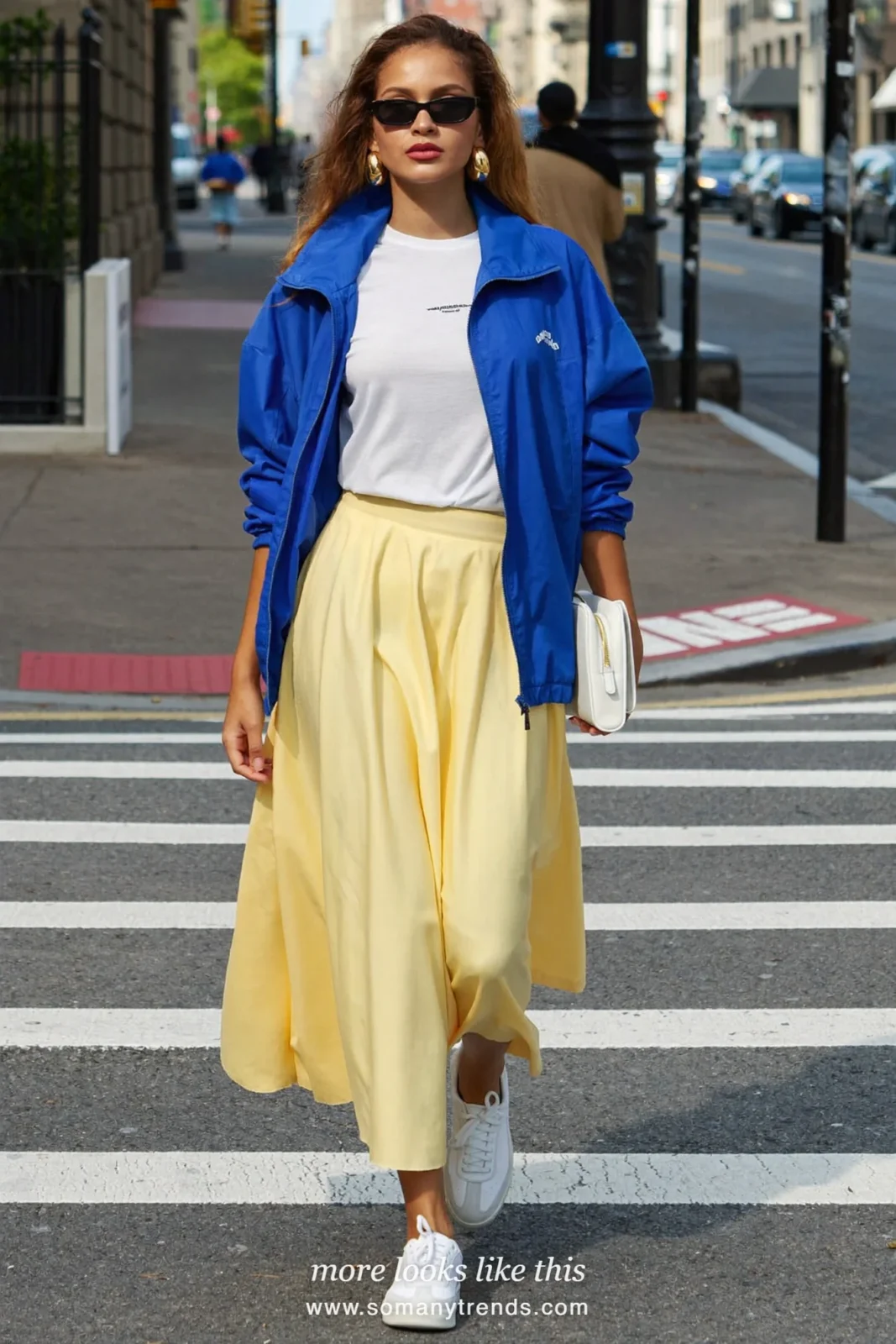Woman in a cobalt blue windbreaker, white tee, butter yellow midi skirt and white sneakers on a New York sidewalk, outfit 4