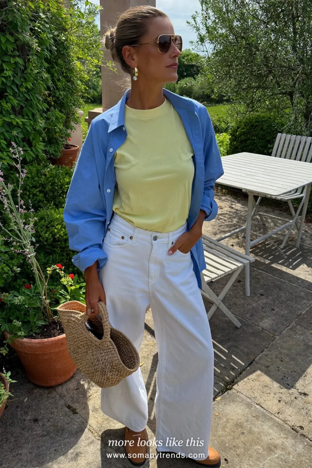 Woman in an open cornflower blue cotton shirt over a butter yellow tee, white jeans and tan loafers in a country-house garden, outfit 5