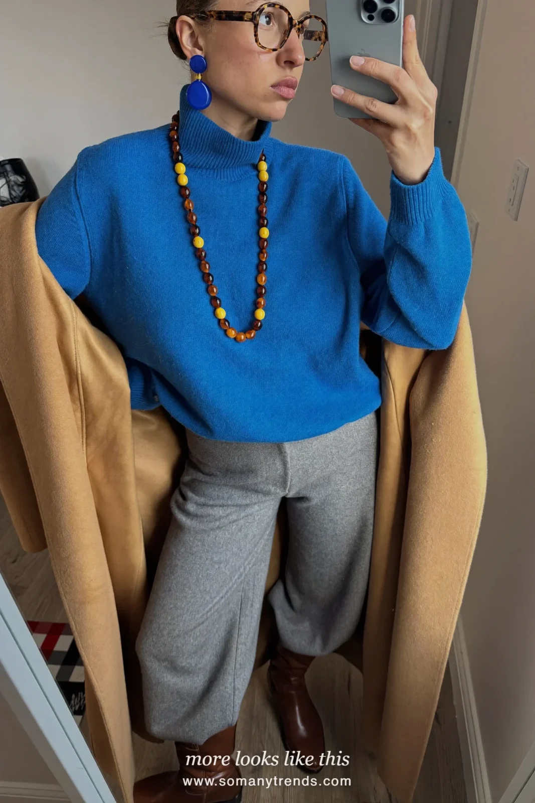 Woman in a cobalt blue merino turtleneck, camel long coat, gray wide-leg pants, brown boots and a lemon yellow top-handle bag, outfit 6