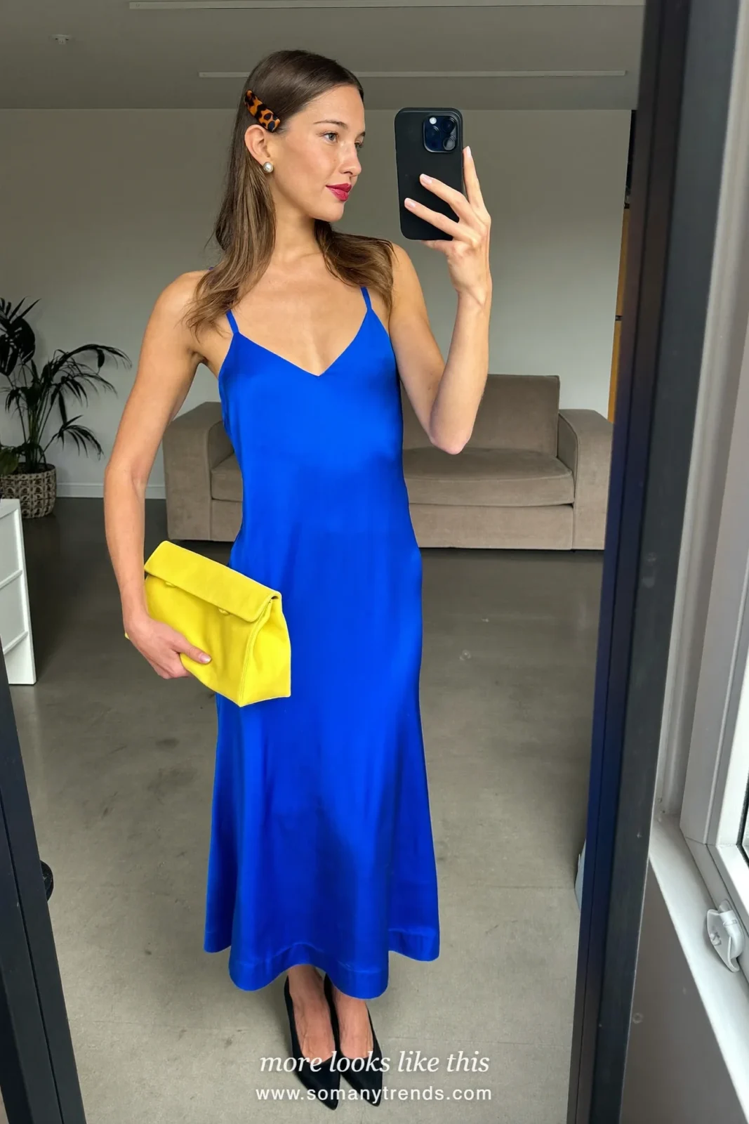 Woman in a cobalt blue satin slip midi dress, sheer black tights, black pointed pumps and a lemon yellow clutch at a bar entrance, outfit 12